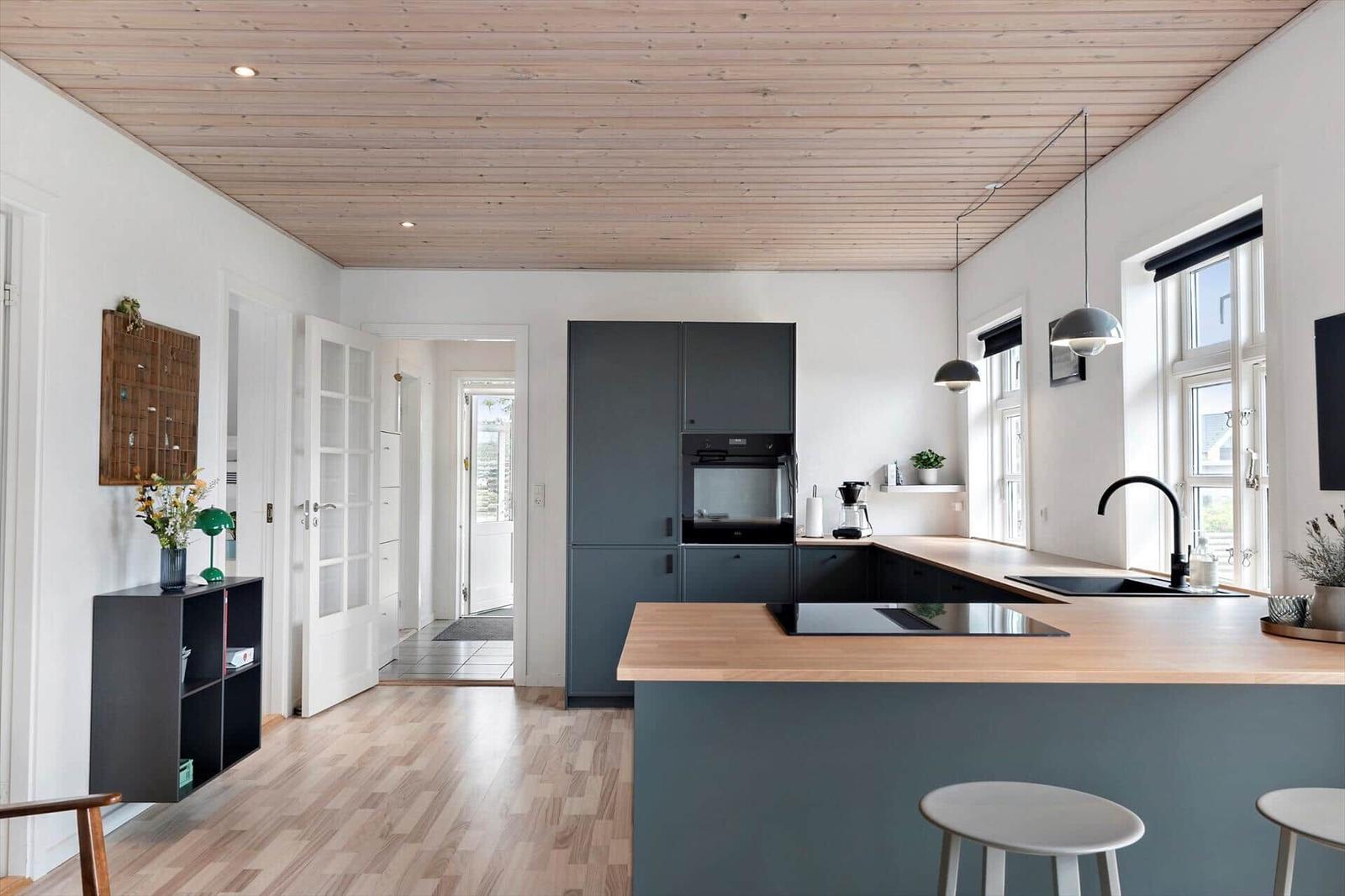 Küche mit Holzdecke, dunklen Schränken und Holz Arbeitsplatte. Fenster und Barhocker sind sichtbar.