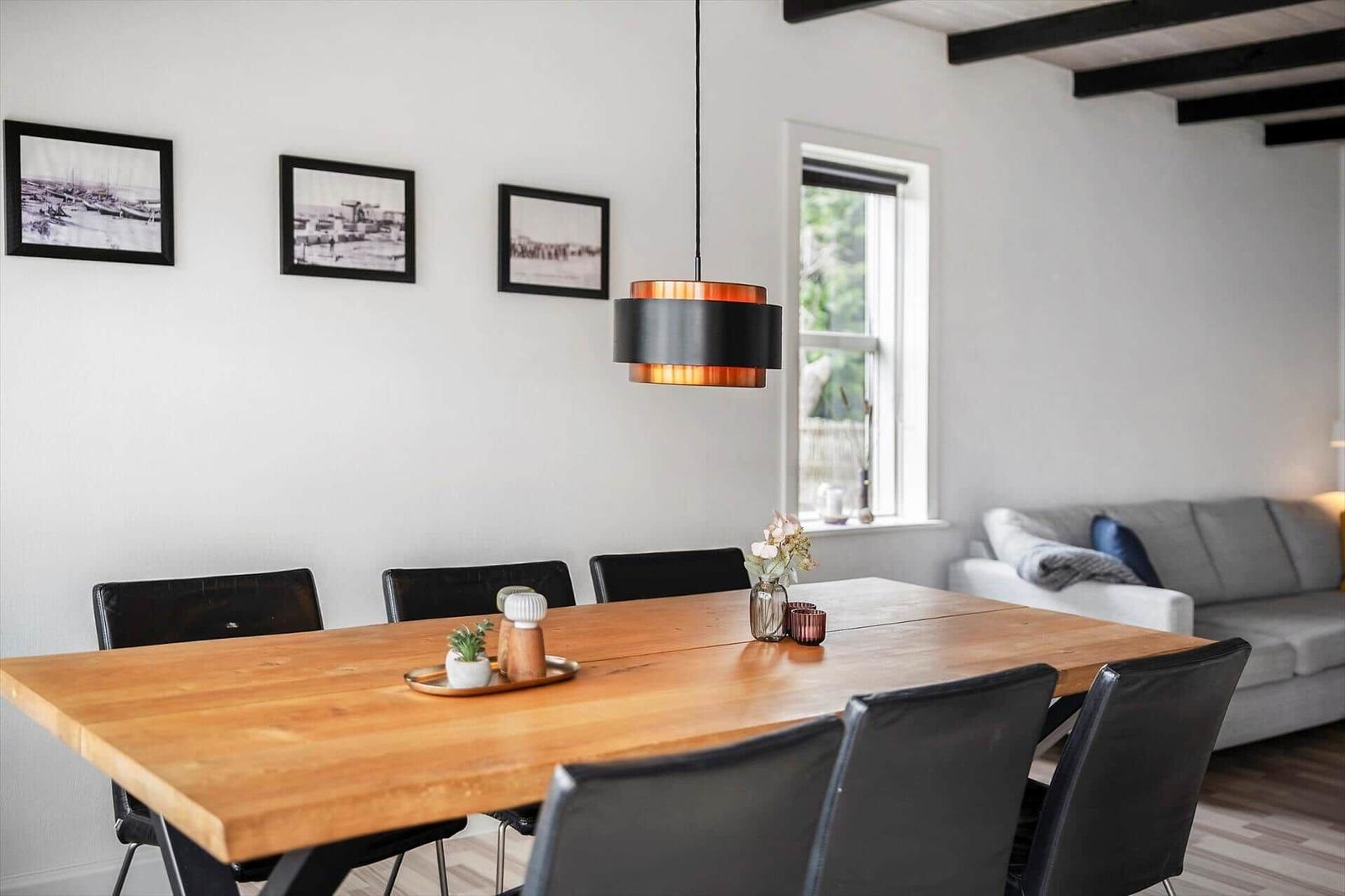 Esszimmer mit Holztisch, schwarzen Stühlen und Wandbildern. Wohnbereich mit Sofa im Hintergrund.