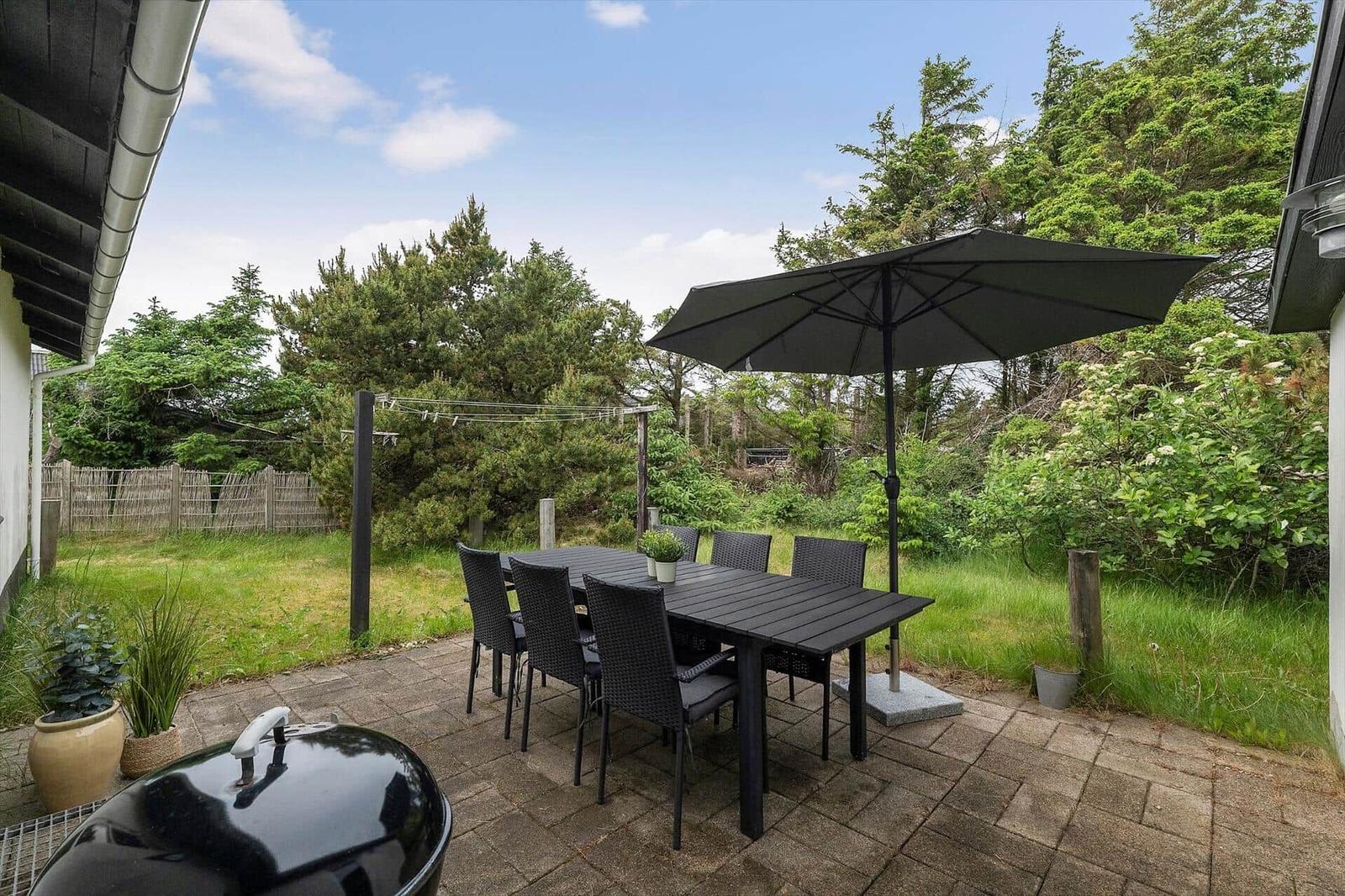 Terrasse mit Tisch, sechs Stühlen und Sonnenschirm. Grill und Pflanzen sind vorhanden.