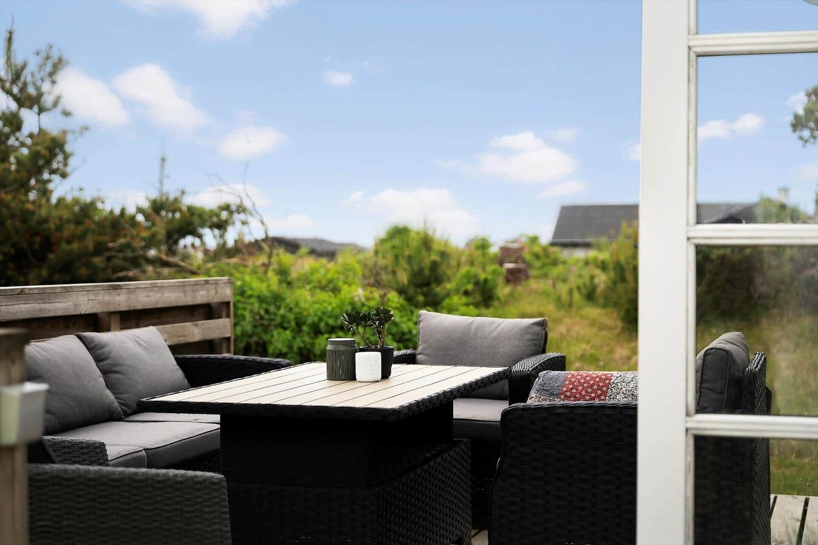 Terrasse mit Sitzgruppe und Tisch. Blick auf Grünfläche und Himmel.