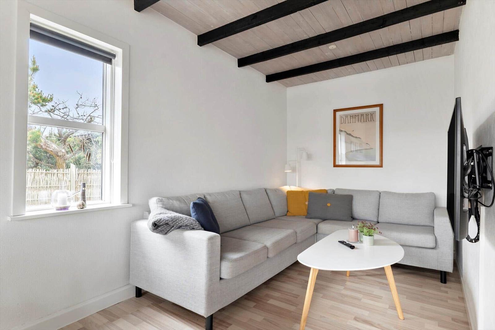 Wohnzimmer mit grauem Sofa, weißem Tisch und Fensterblick auf Garten.