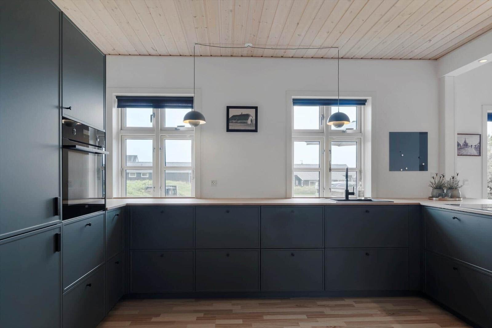 Moderne Küche mit dunklen Schränken, Holzboden und großen Fenstern.