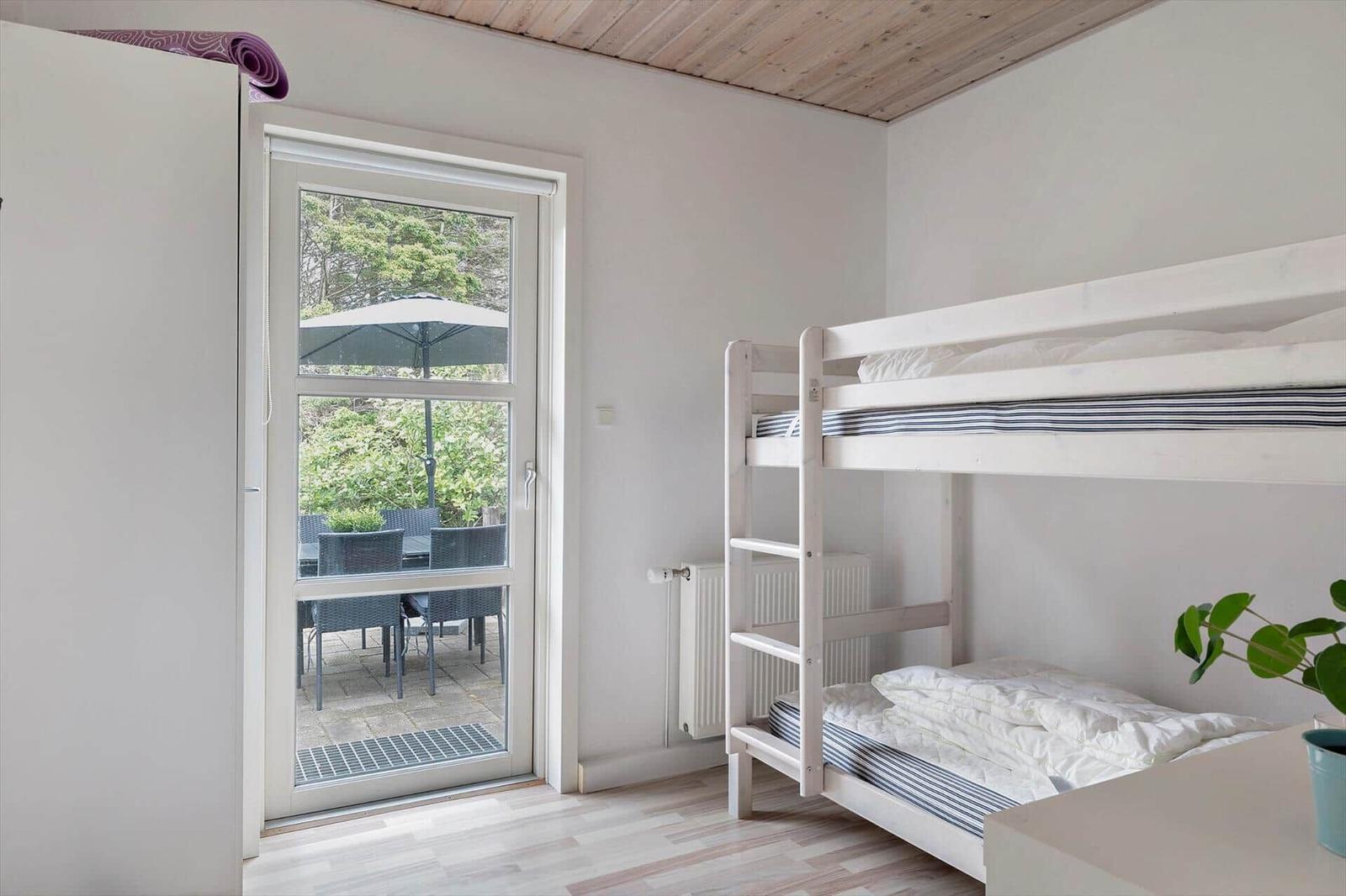 Zimmer mit Doppelstockbett und Fenster zur Terrasse mit Sitzgelegenheit.