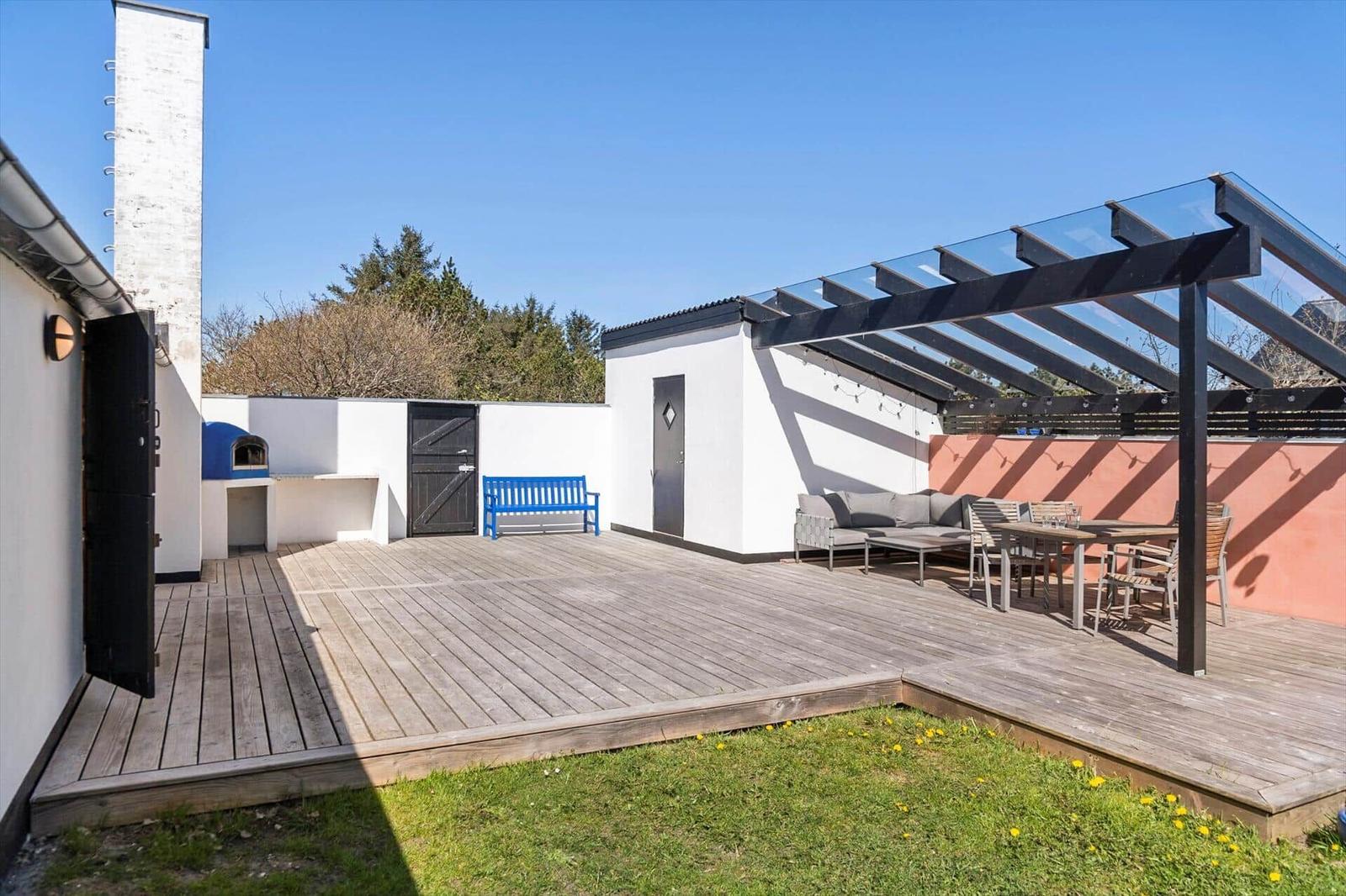 Terrasse mit Holzdecke, Sitzgruppe und Sonnenschutz. Grillbereich und Garten sind sichtbar.