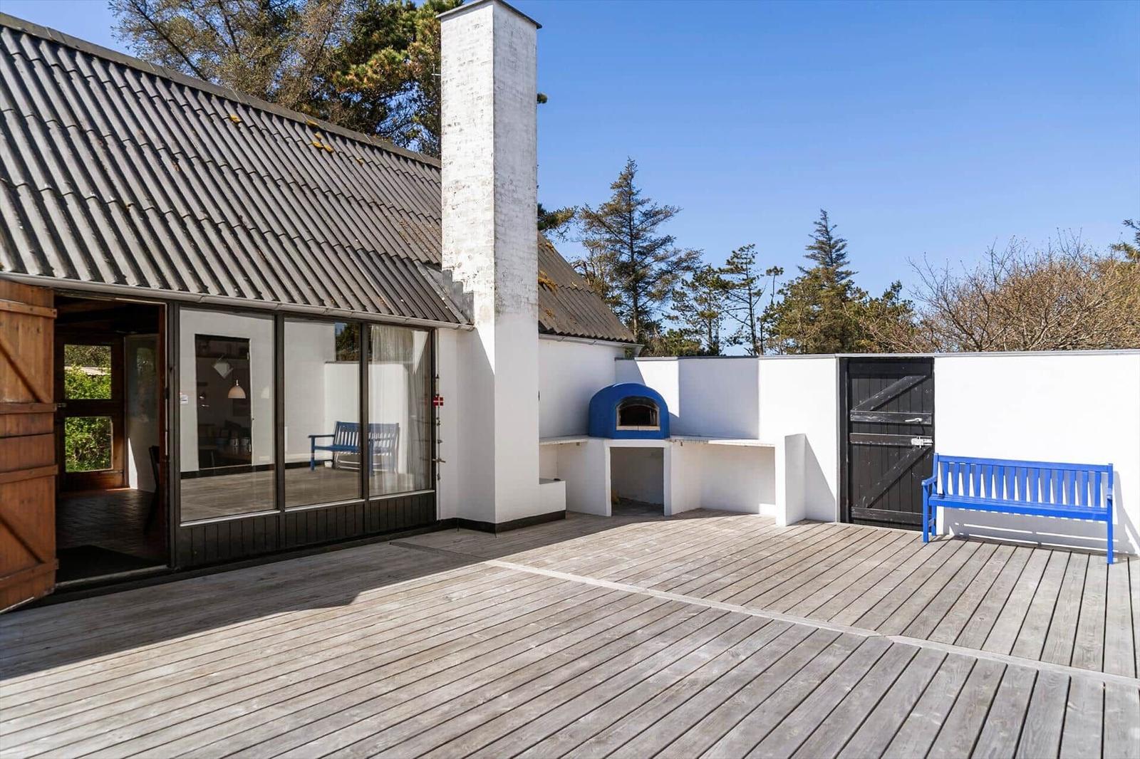 Terrasse mit Holzdecke, blauer Bank und integriertem Ofen neben weißer Wand.