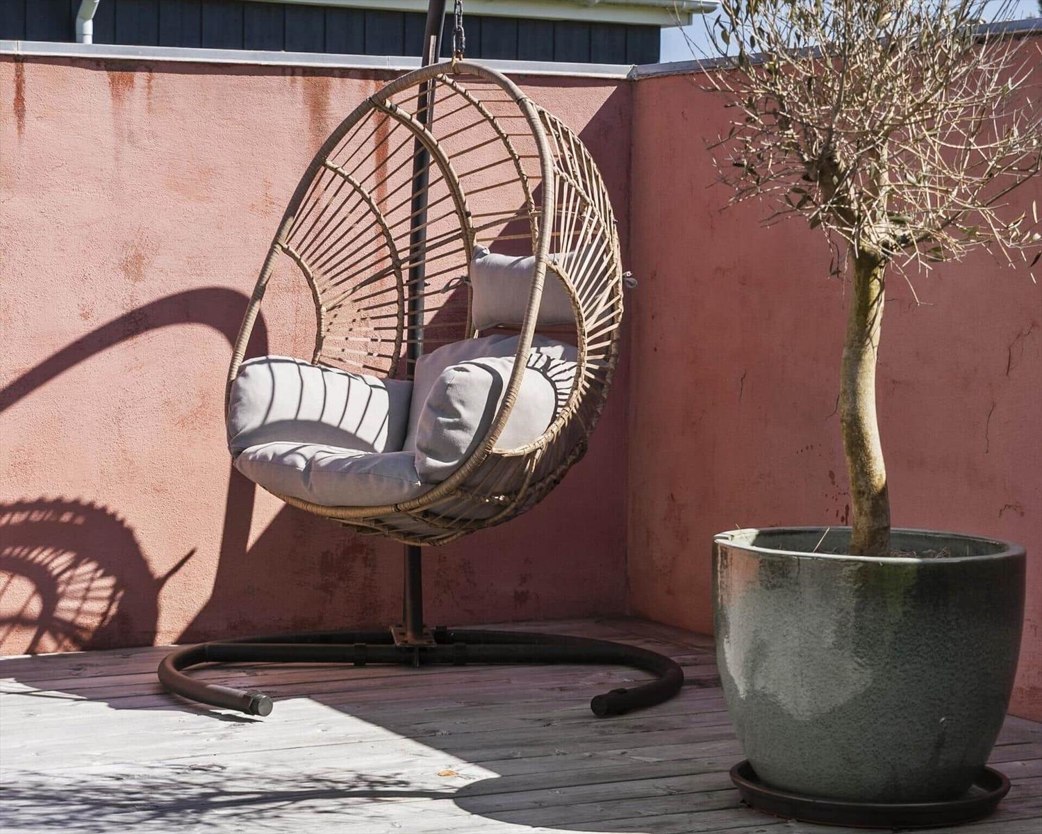 Hängesessel mit Kissen auf Terrasse neben Pflanze in Topf.