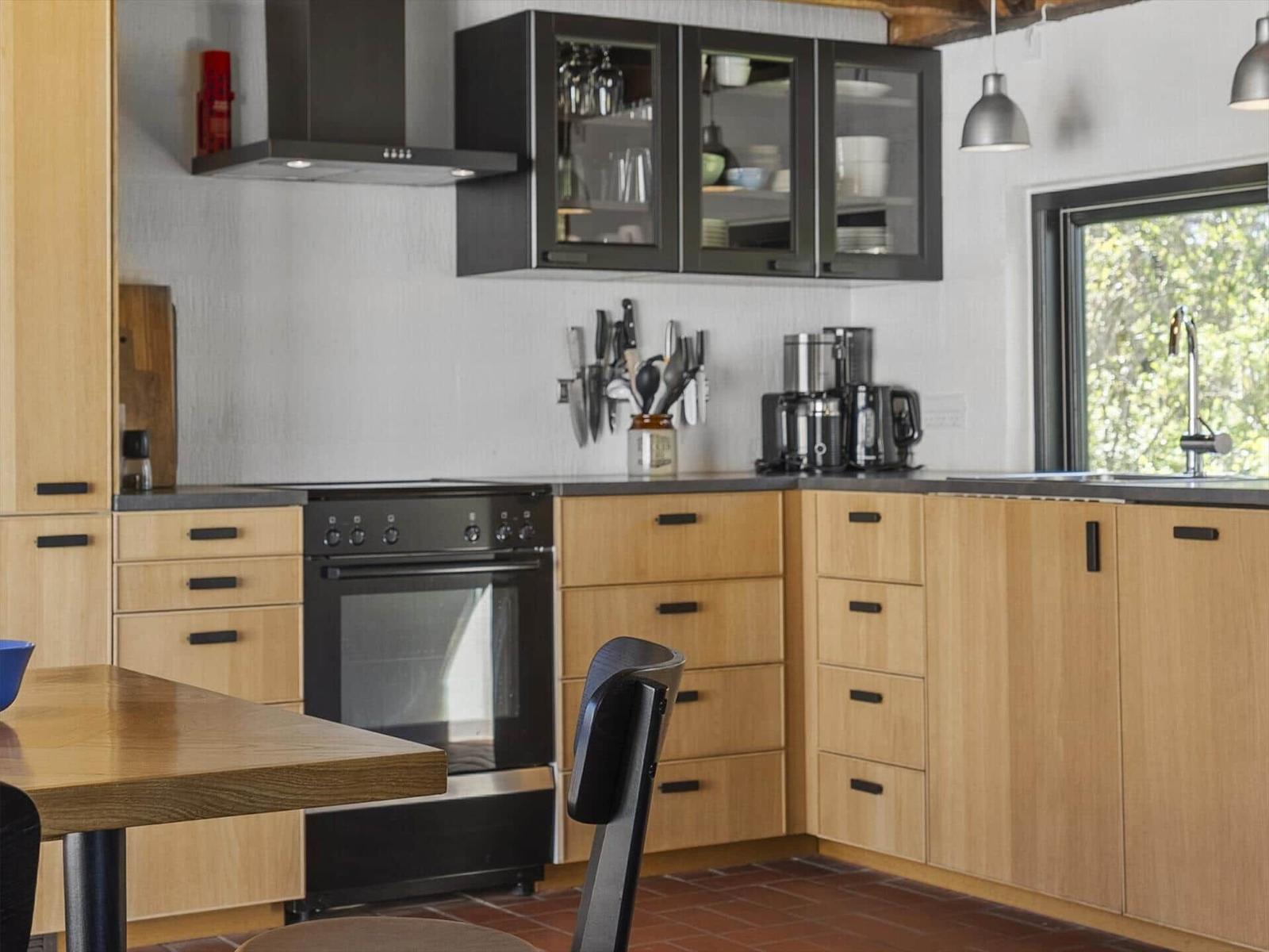 Moderne Küche mit Holzschränken, schwarzer Kochplatte und Fenster zum Garten.