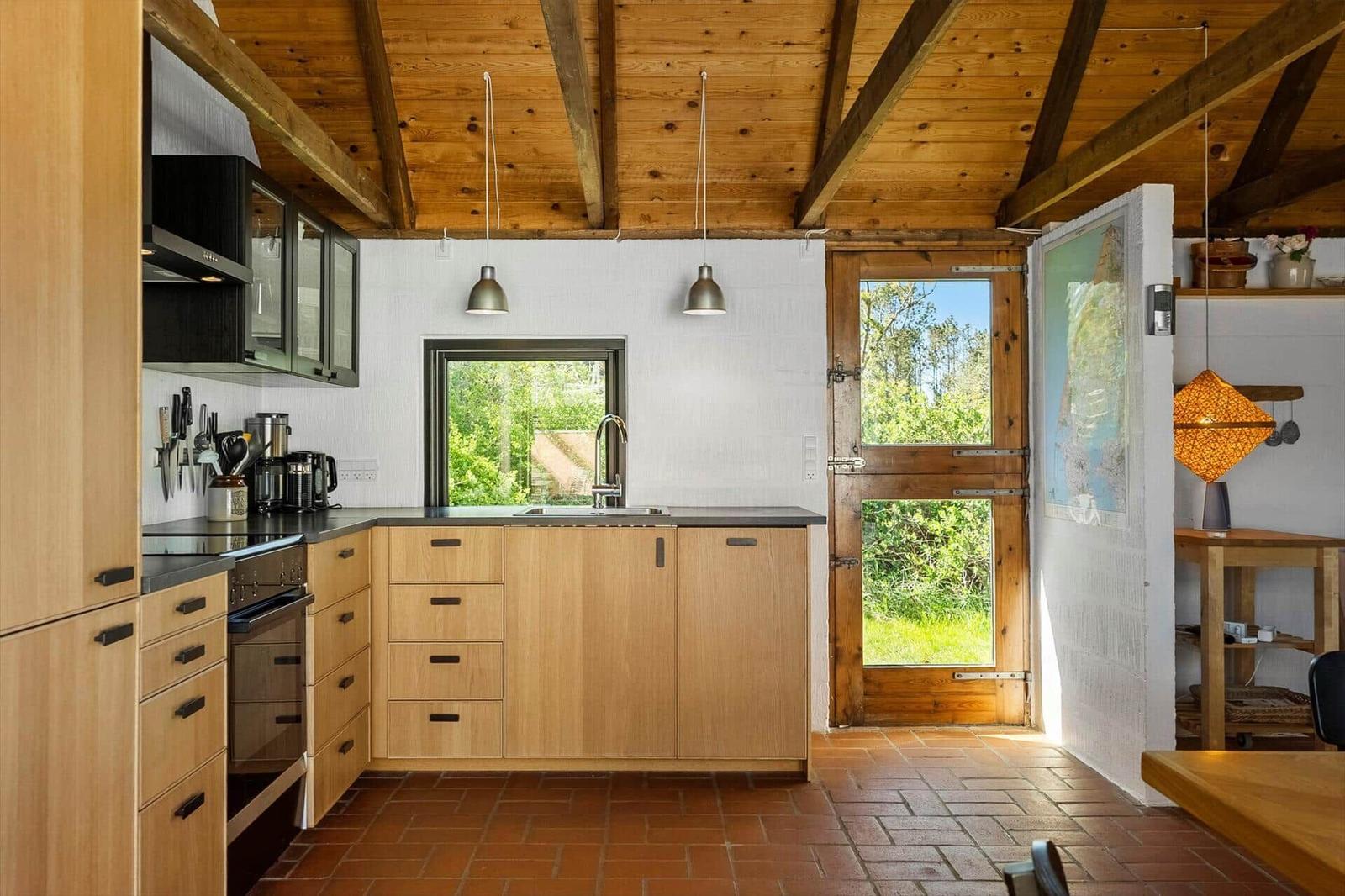 Küche mit Holzdecke, Fenster und Tür zum Garten. Arbeitsfläche, Spüle und Kochgeräte.