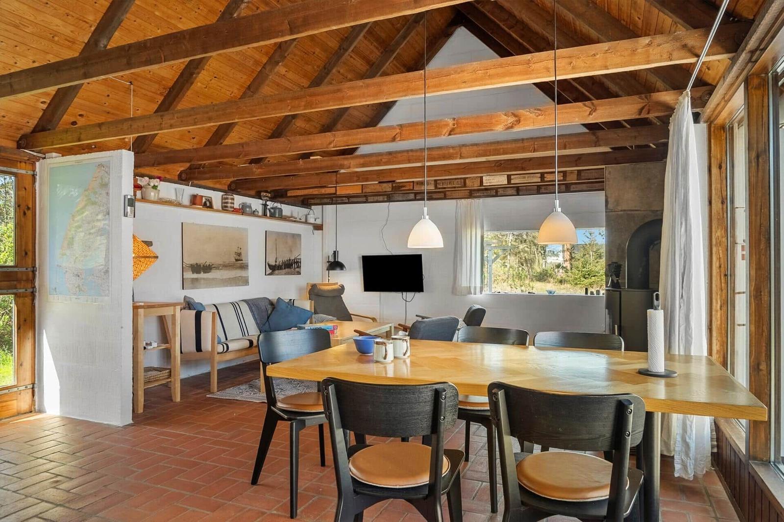 Großer Raum mit Holzdecke, Esstisch und Sofa. Fenster bieten Blick auf Außengelände.