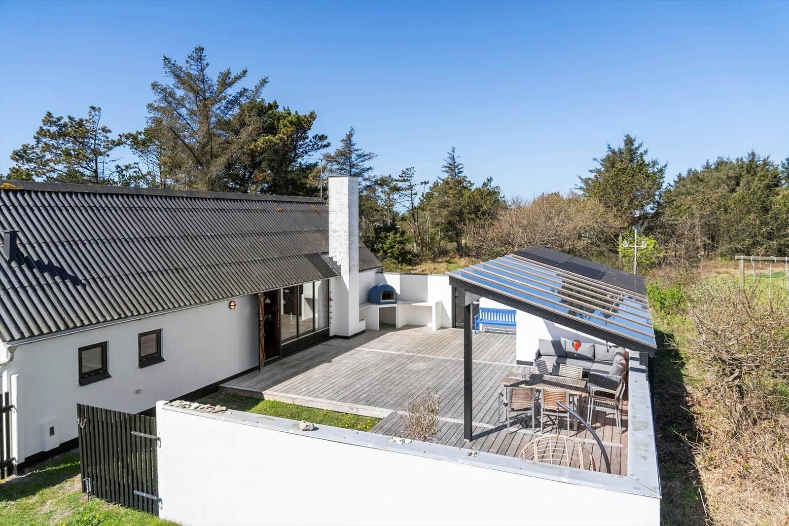 Moderne Villa mit Terrasse, Grill und Garten. Umgeben von Bäumen unter blauem Himmel.