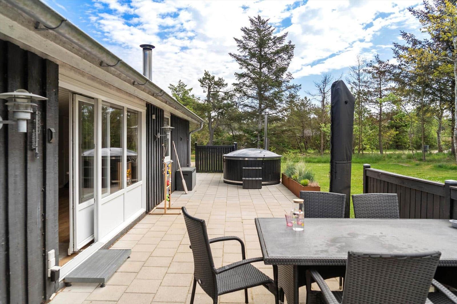 Terrasse mit Sitzgruppe, Whirlpool und Garten. Holzhaus mit Glastüren und Dach.