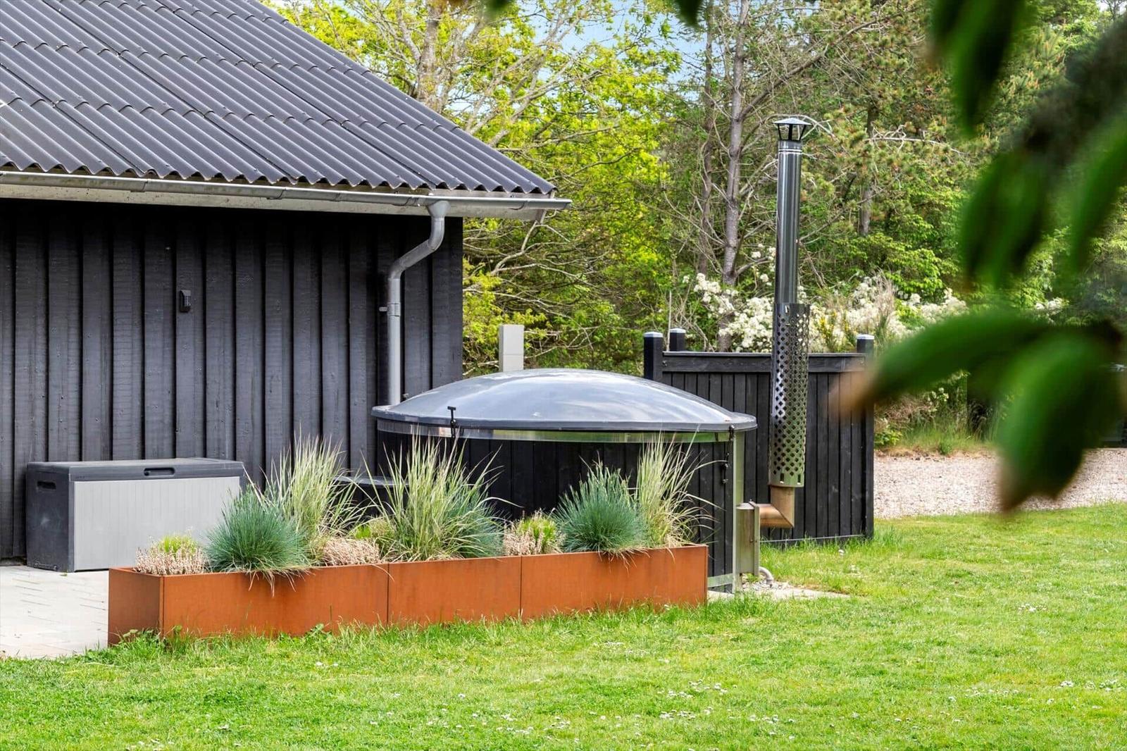 Hinterhof mit Whirlpool, Pflanzenbeet und Garten. Schwarze Holzwand und grünes Gras.