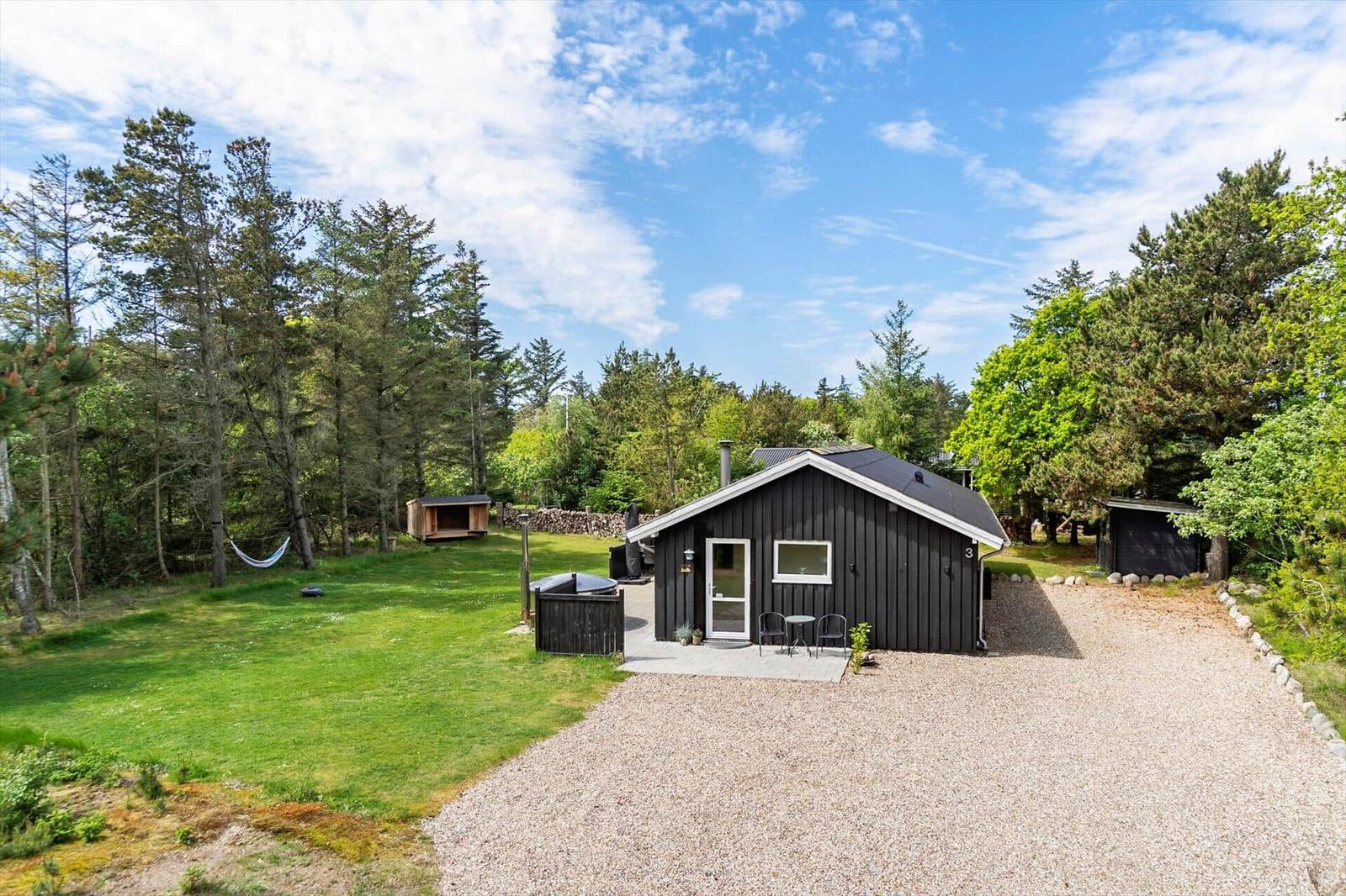 Schwarzes Holzhaus mit Garten, Terrasse und Grillplatz zwischen Bäumen.