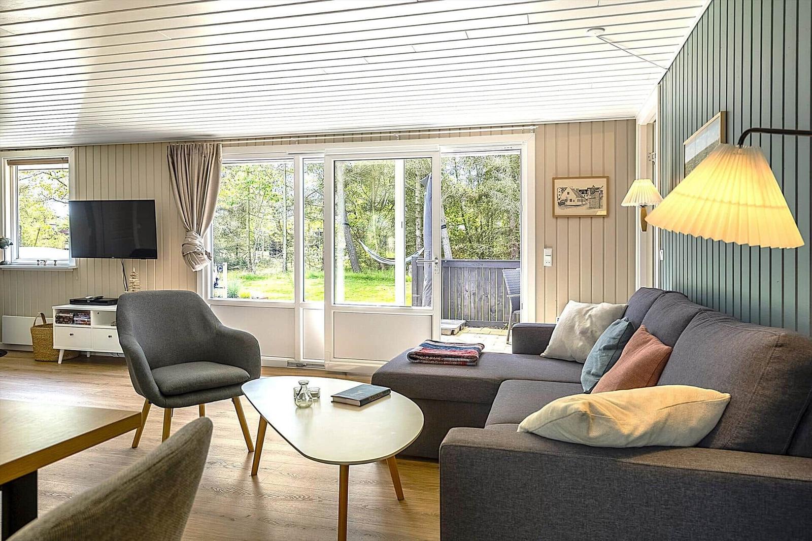 Wohnzimmer mit Sofa, Sessel und TV. Durchgang zum Balkon mit Blick auf Grün.