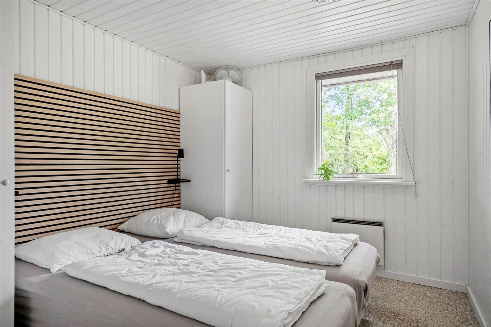 Zwei Betten mit weißen Bettwäschen, Holzpaneelen an der Wand und Fenster mit Blick auf Bäume.