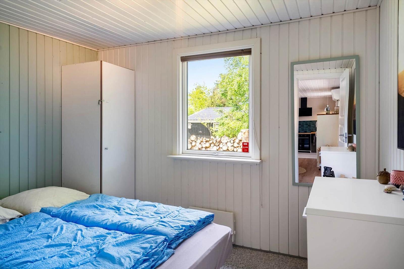 Schlafzimmer mit Bett, Kleiderschrank und Fenster zum Garten.