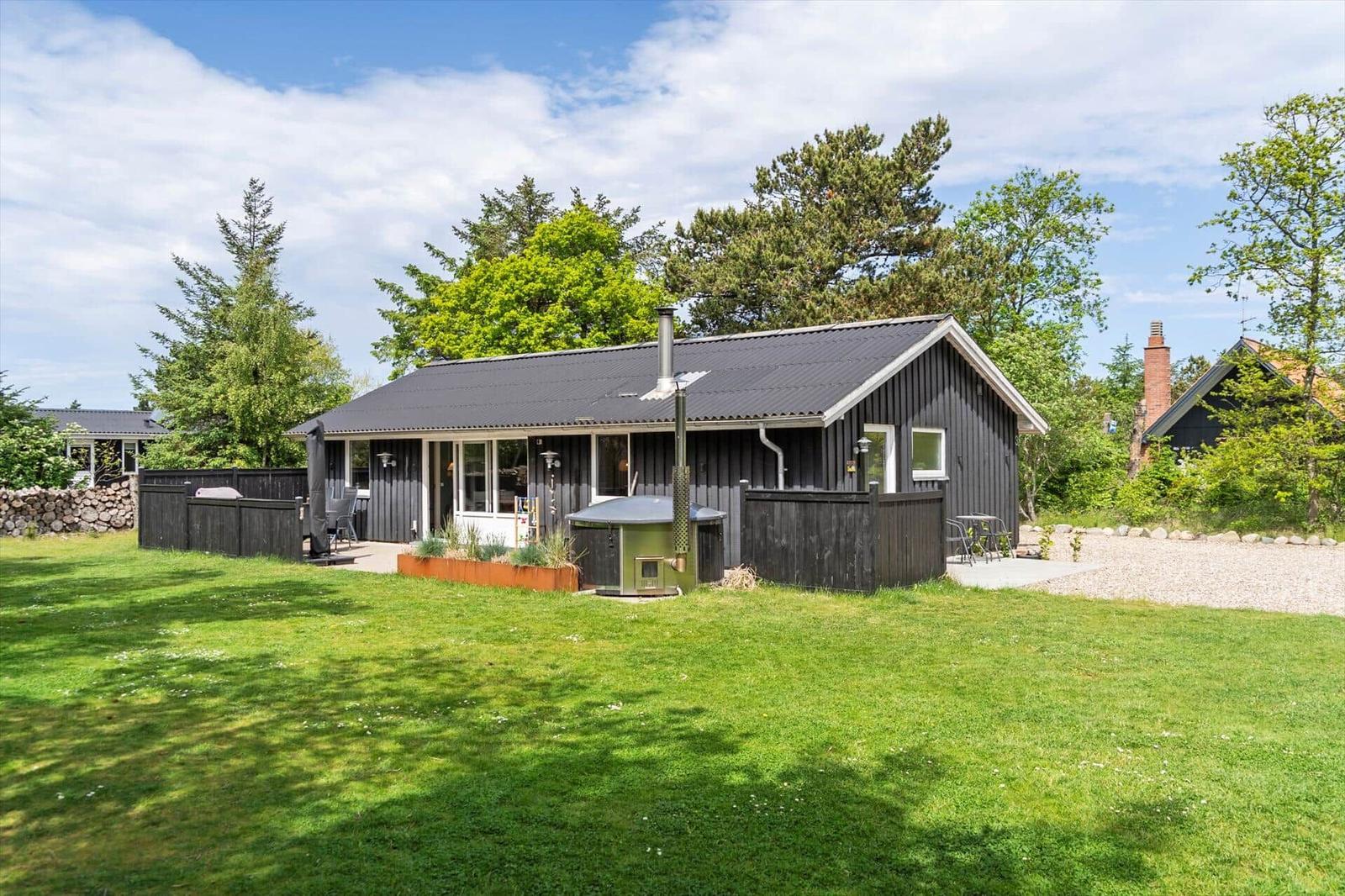 Schwarzes Holzhaus mit Terrasse, Garten und Sauna im Freien.