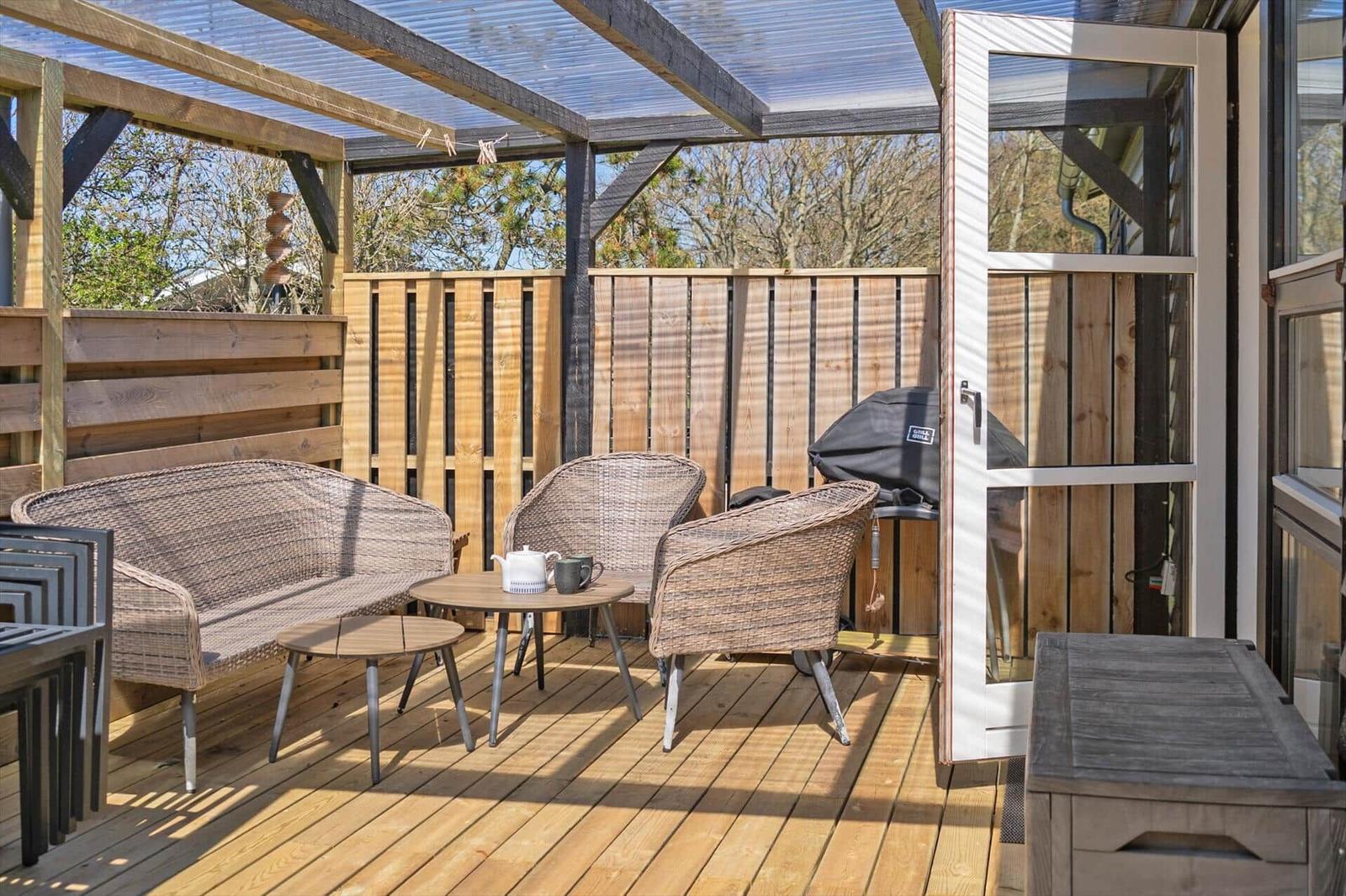 Terrasse mit Sitzgruppe, Grill und Holzverkleidung. Durchgehendes Dach und Holzdielenboden.