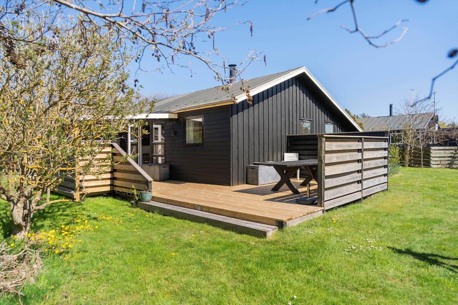 Schwarzes Holzhaus mit Terrasse und Garten. Tisch und Stühle auf der Terrasse.