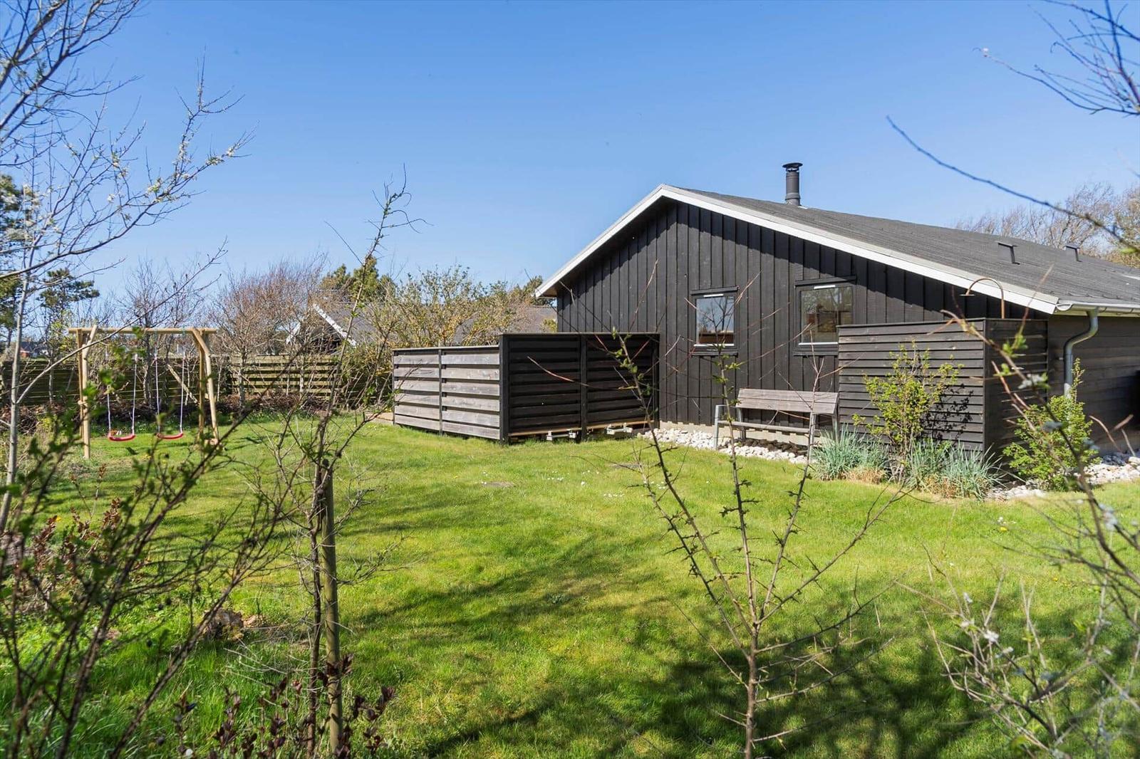 Ein dunkel lackiertes Haus mit Garten, Schaukel und Bank.