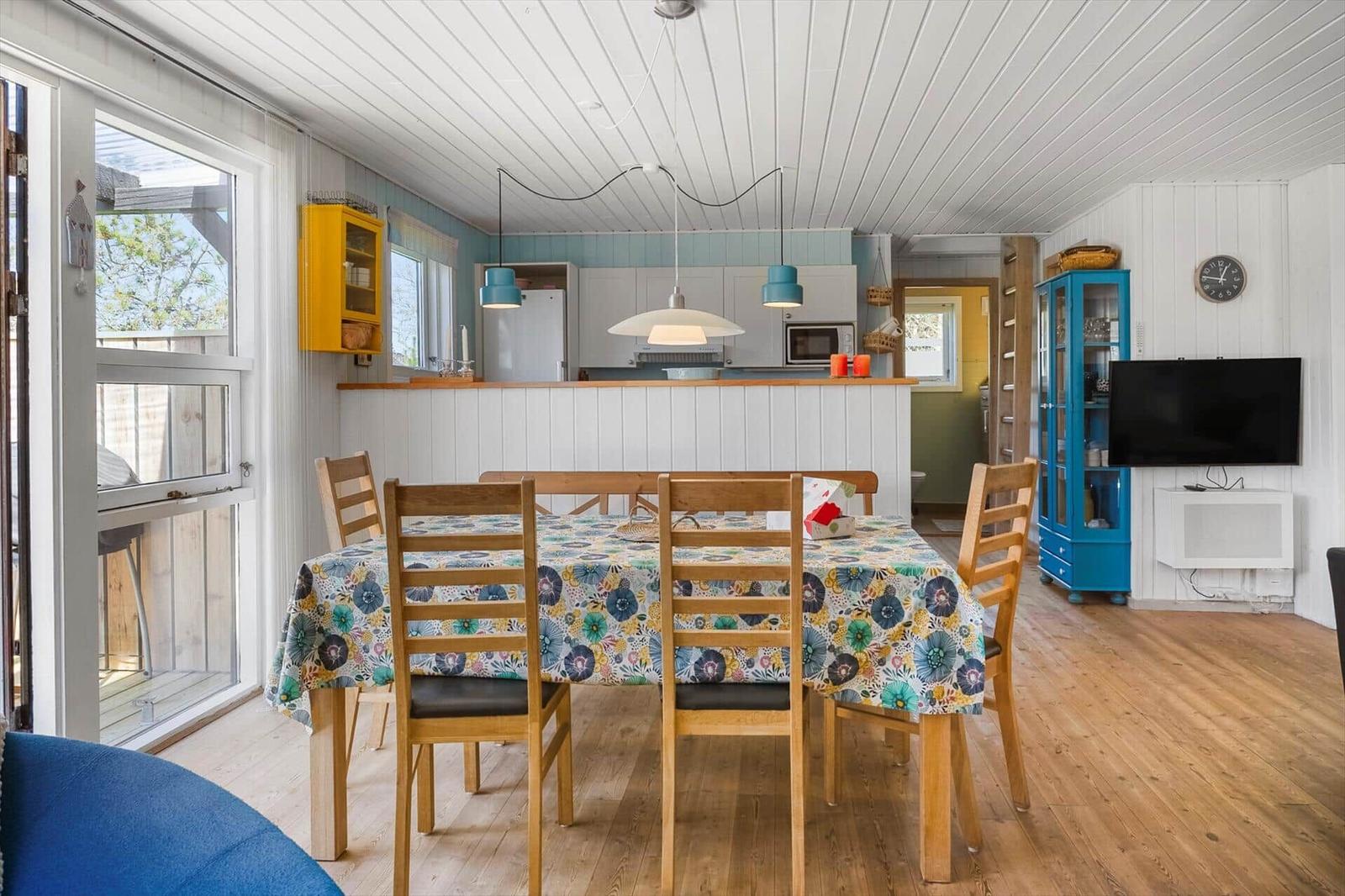 Esszimmer mit Holztisch, blauem Tischtuch und Küchenbereich im Hintergrund.