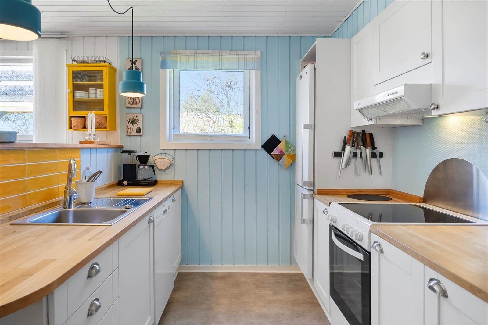 Küche mit weißen Schränken, Holzoberflächen und blauen Wänden. Fenster, Spüle, Herd und Kühlschrank sichtbar.