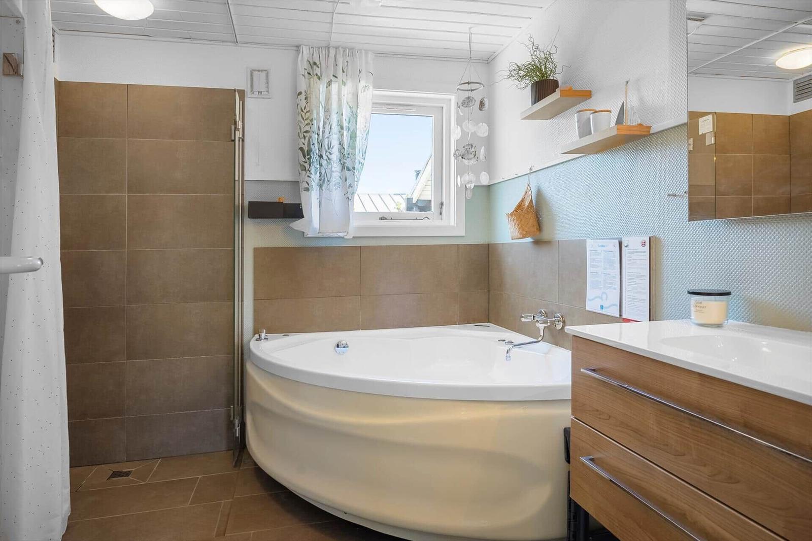 Bad mit Whirlpool, Fenster, Waschbecken und Holzschrank.