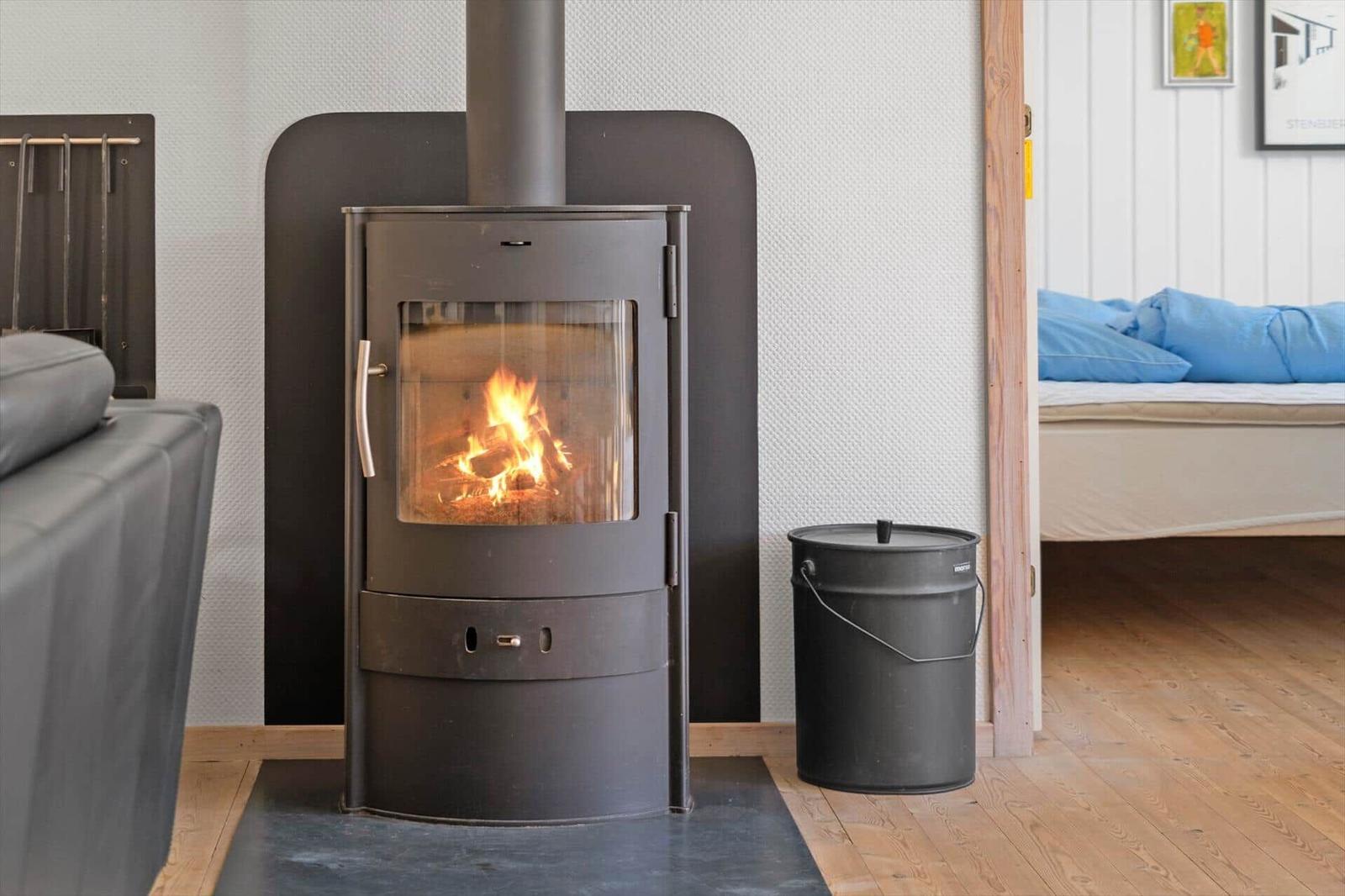 Kaminofen mit brennendem Feuer, daneben Eimer und Bett im Hintergrund.