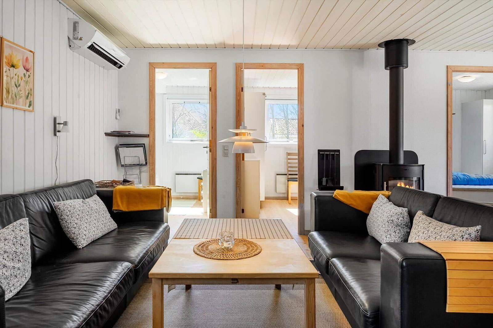 Wohnzimmer mit zwei schwarzen Sofas, Holztisch und Kaminofen. Durchgänge zu anderen Räumen.