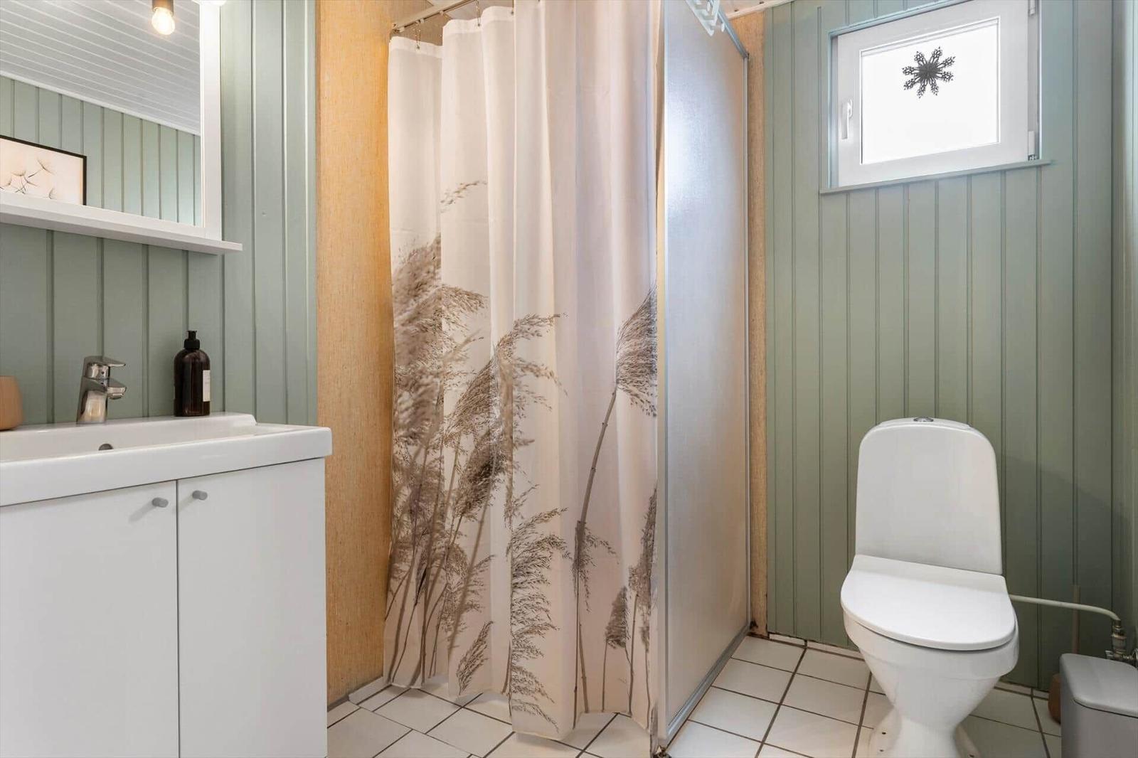 Bathroom with shower, toilet, and sink. Wooden wall and shower curtain with plant motif.