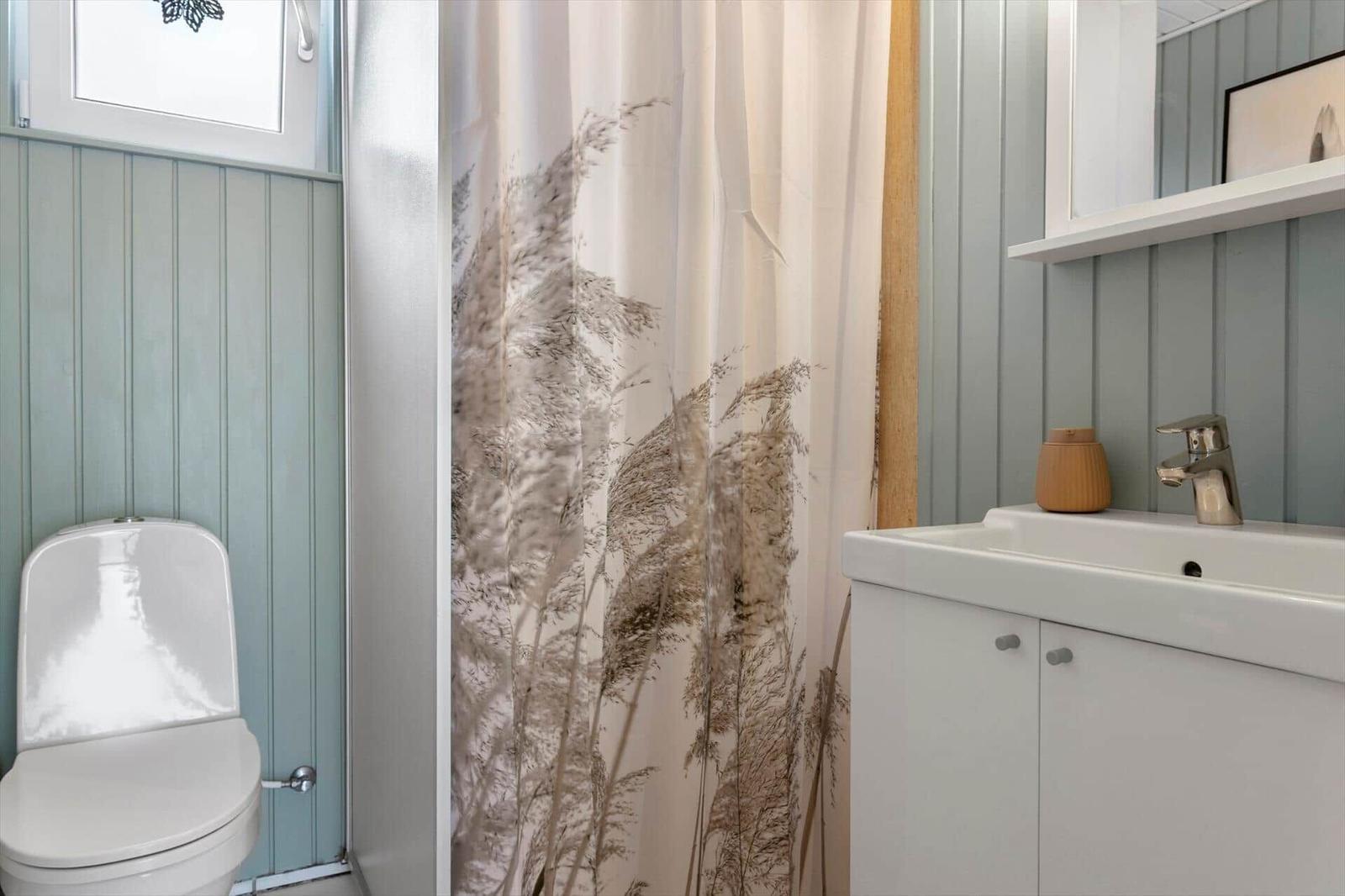 Bathroom with toilet, sink, and shower curtain with plant pattern.