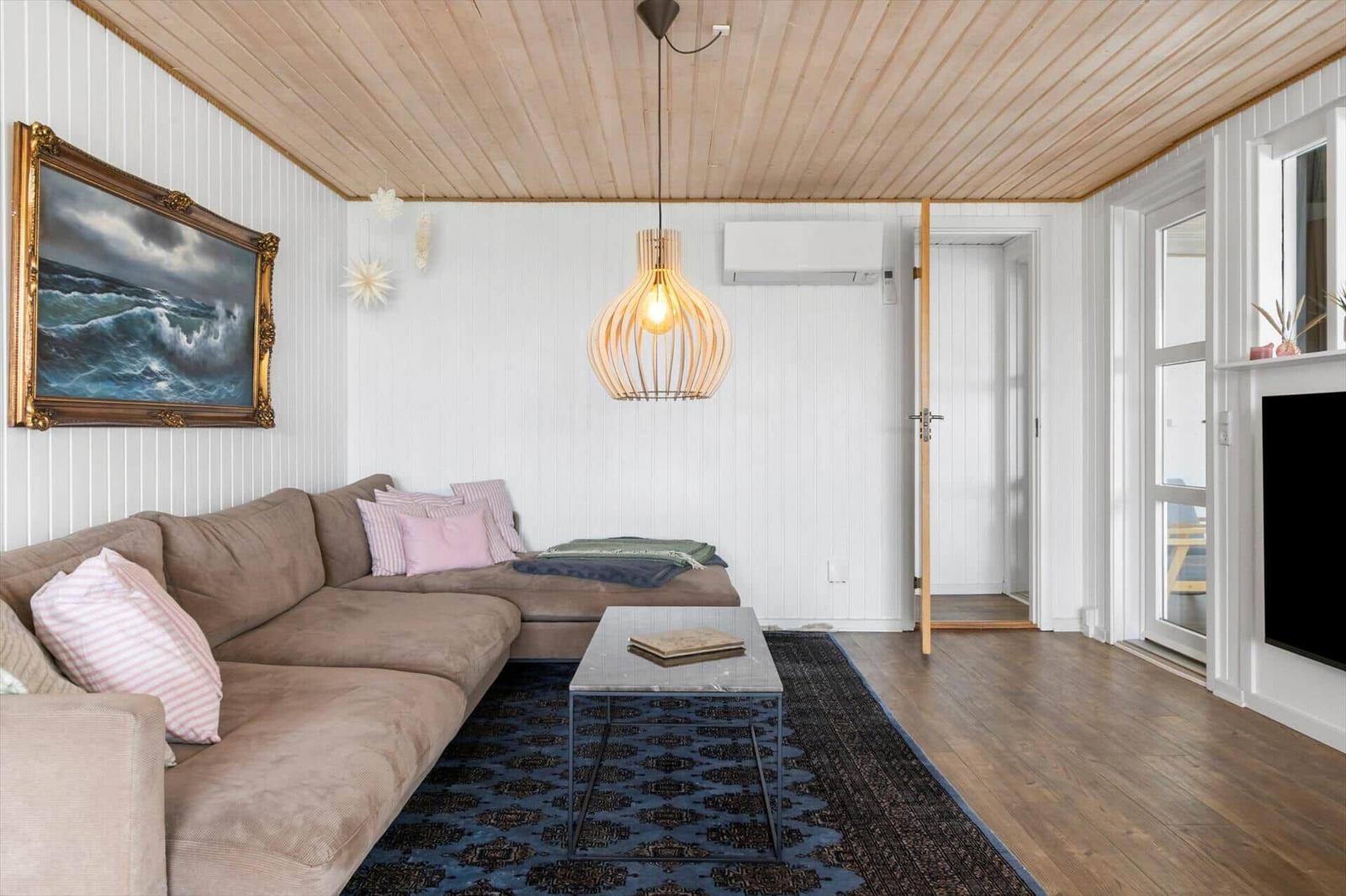 Living room with sofa, rug, and blankets. Wall painting, ceiling lamp, and air conditioner visible.