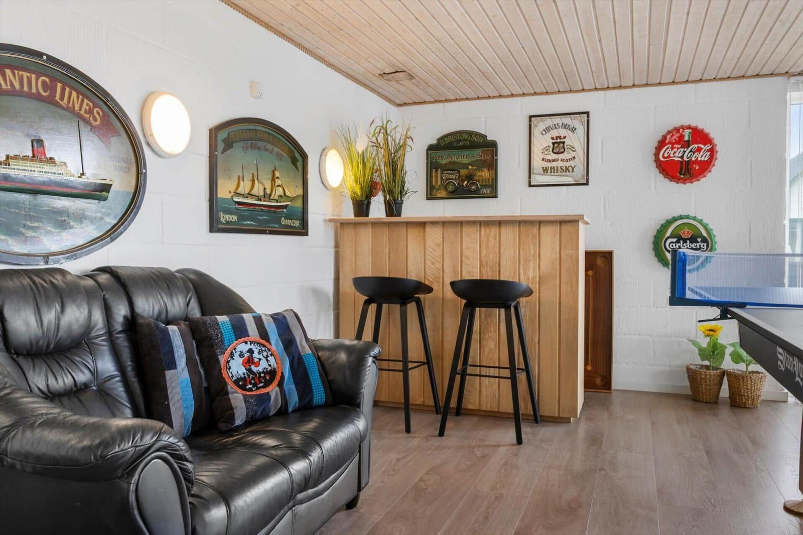 Room with sofa, bar, and ping pong table. Walls with decorations.