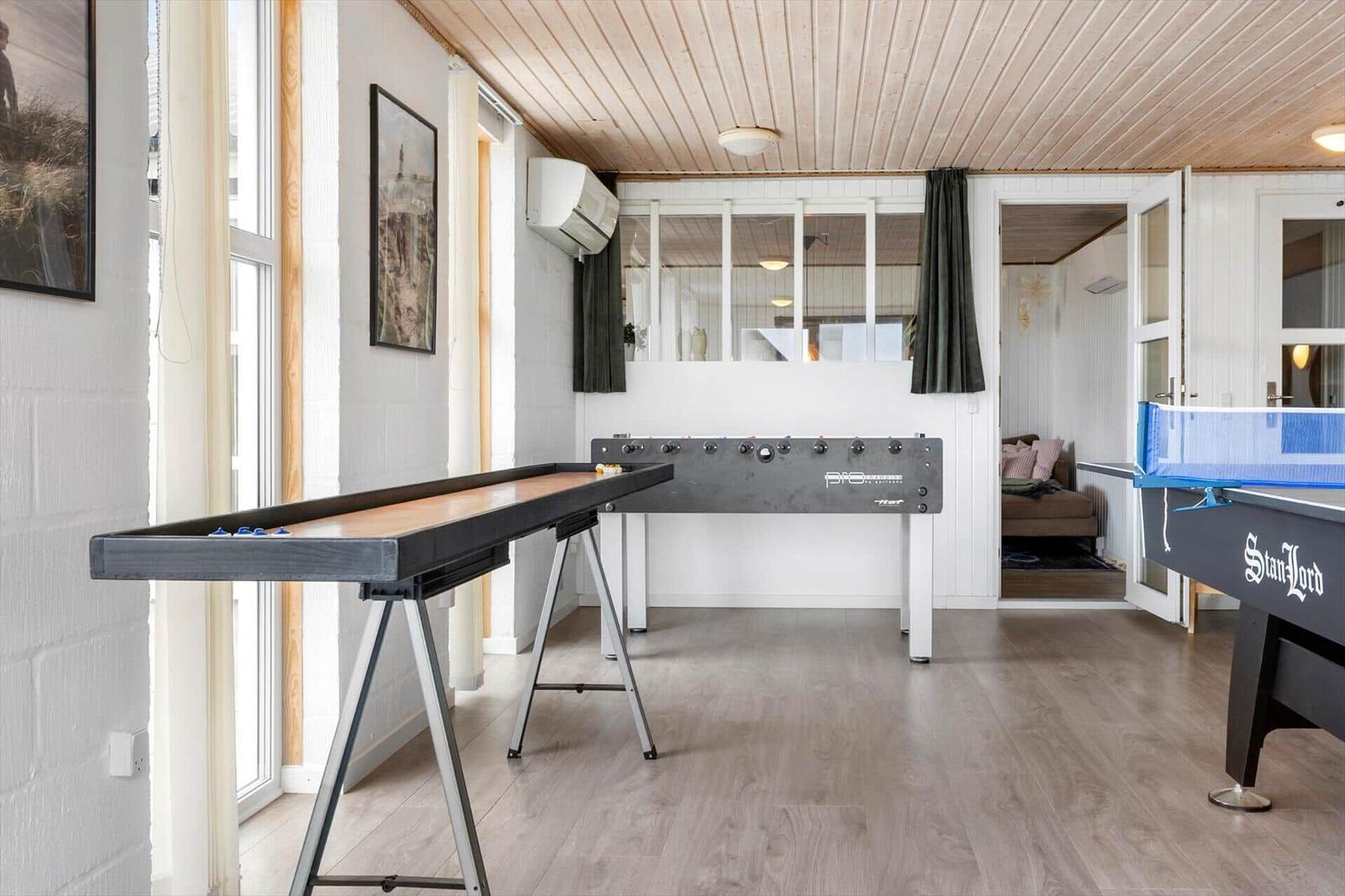 Room with pool table, foosball table, and shuffleboard. Wooden ceiling and light brown floor tiles.