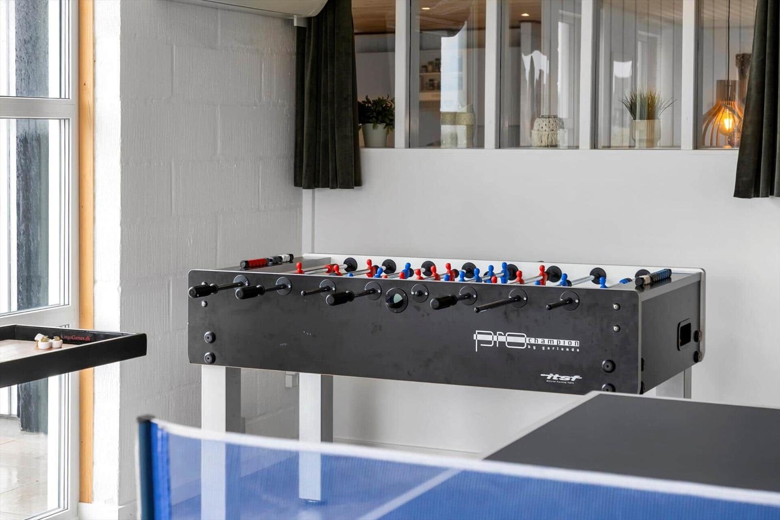 Foosball table with red and blue players near window and wall