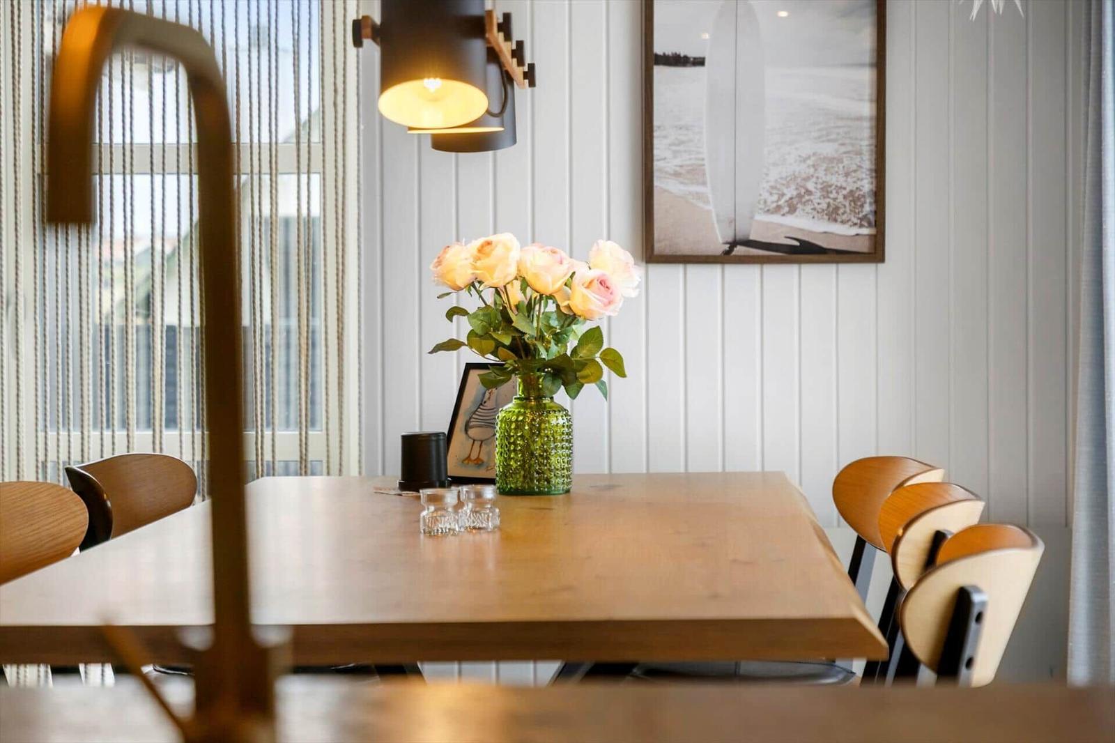 Wooden table with chairs, flowers, and picture on the wall.