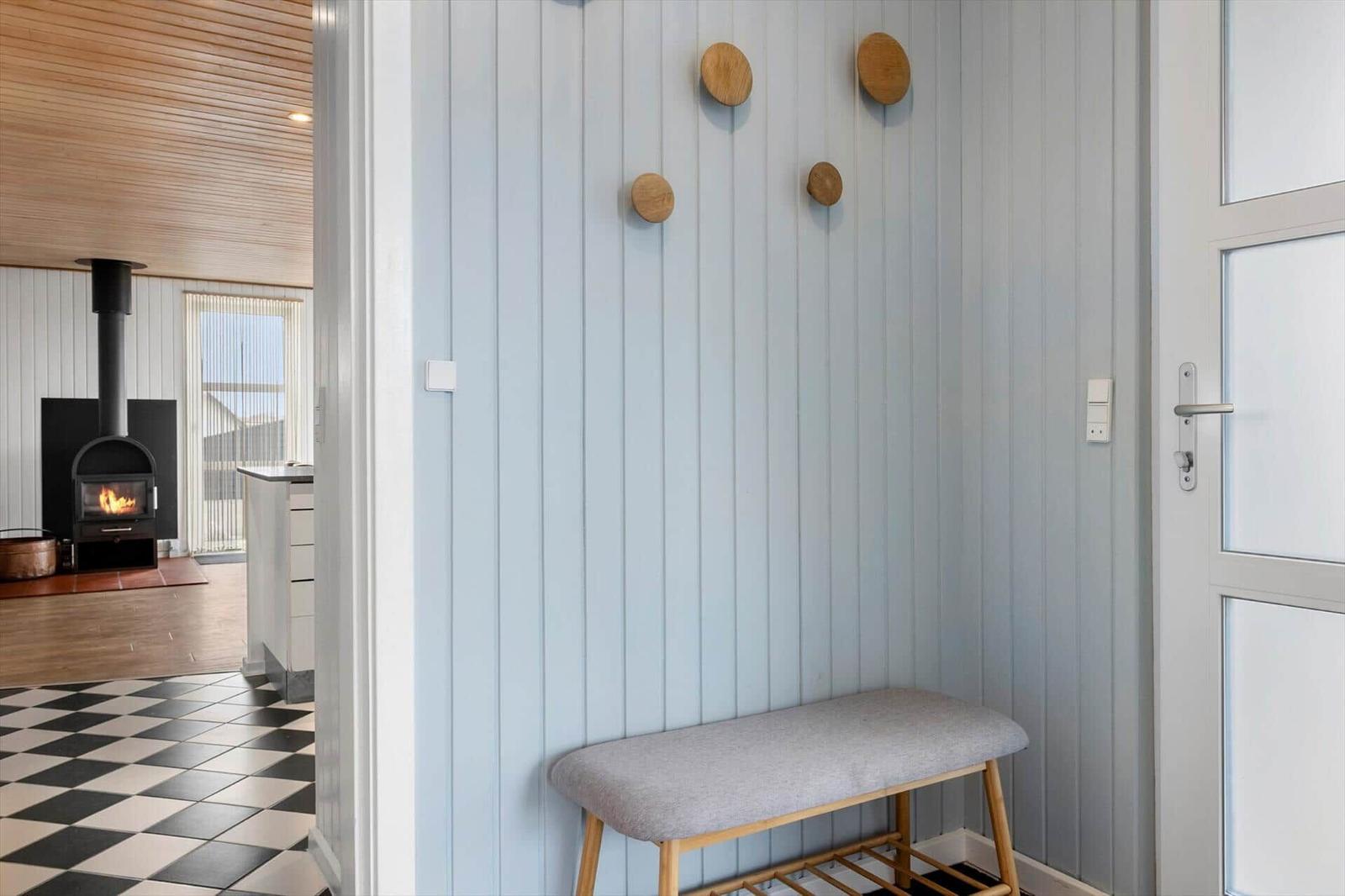 Bright entryway with wooden bench, wall hooks, and view into living area with fireplace.