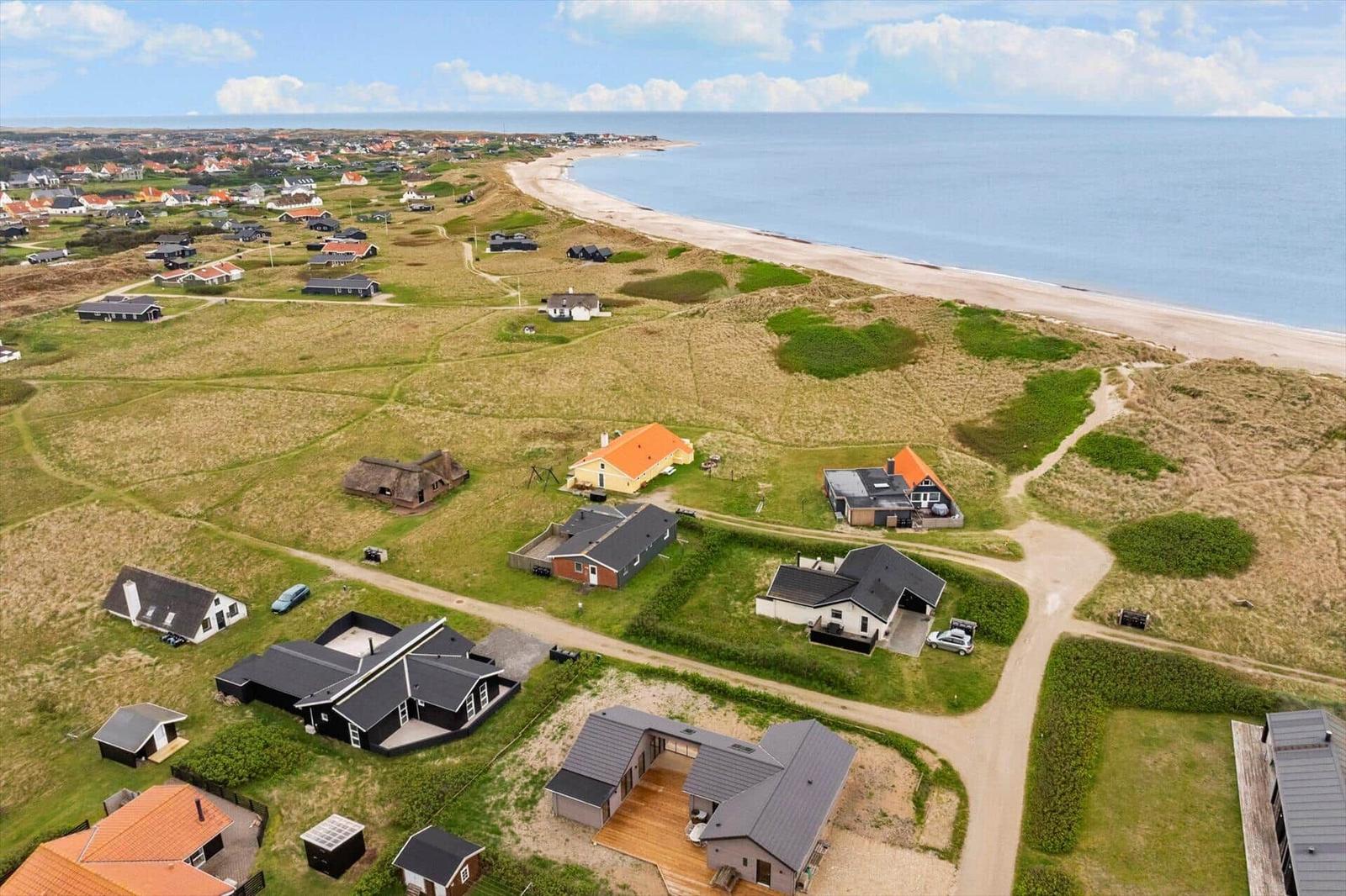 Aerial view of coastal houses with sandy beach and blue sea.