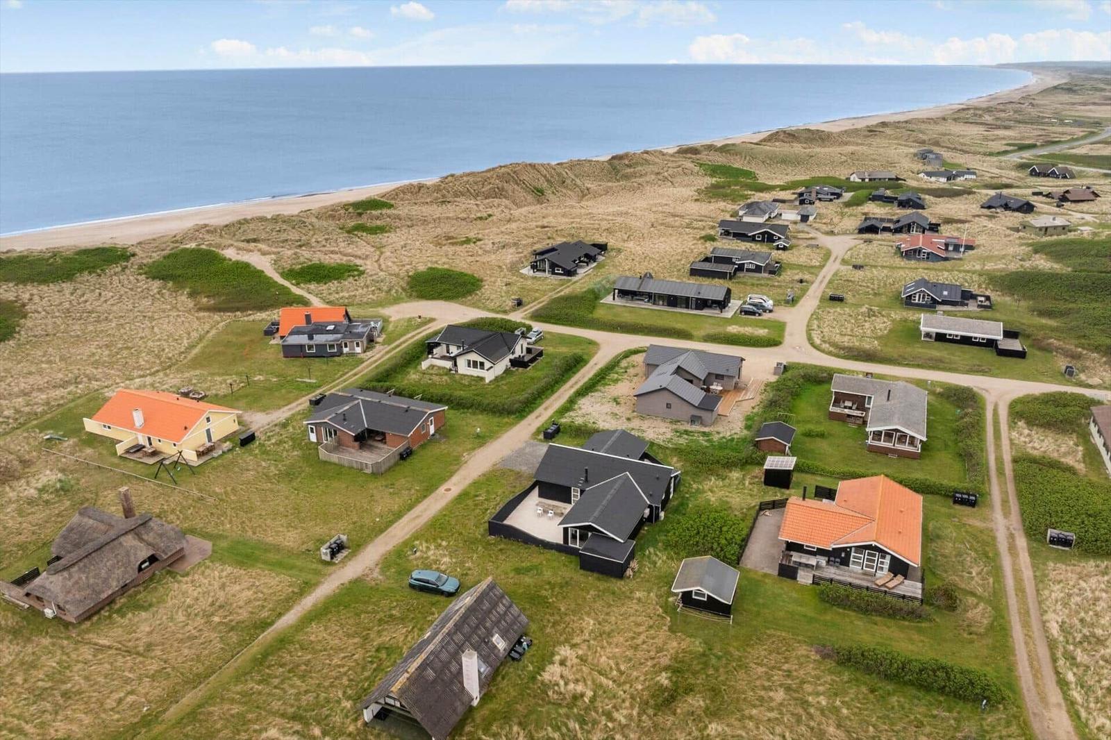 Aerial view of beach houses with dunes and sea in the background.