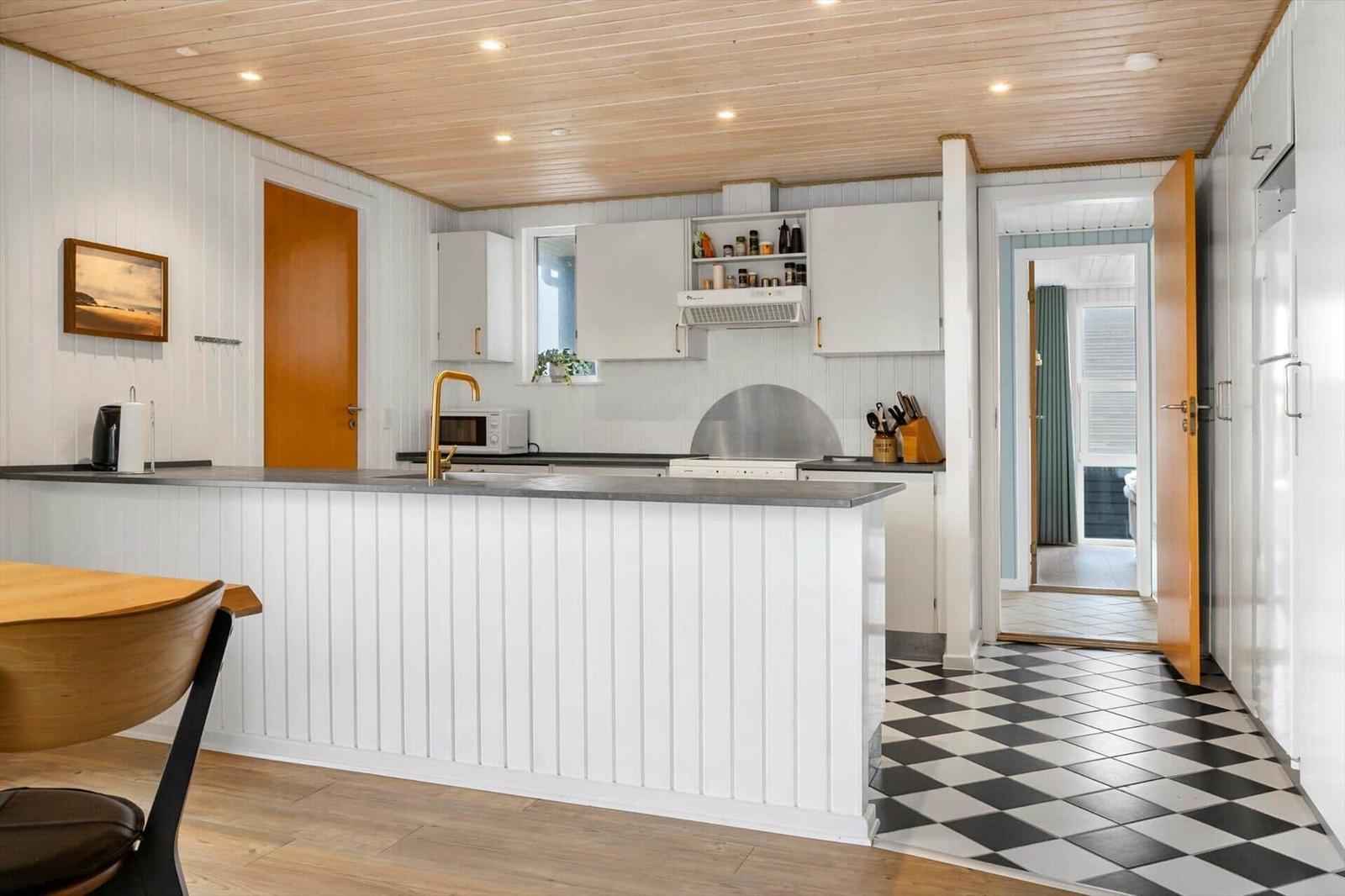 Kitchen with white cabinets, black countertop, and black-and-white tiled floor.