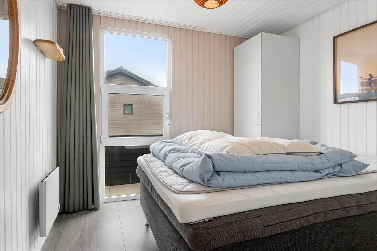 Bedroom with bed, window, and wardrobe. Panelled walls and wooden floor.