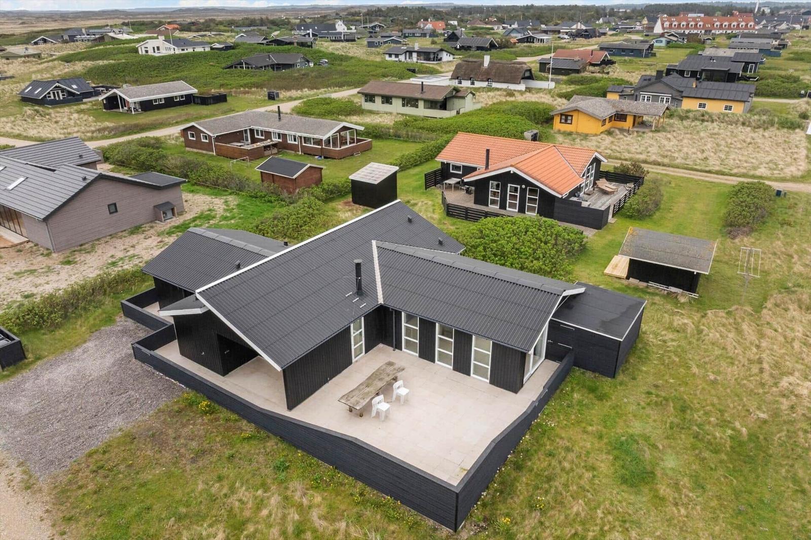 Modern black villa with terrace and garden. Surrounded by other houses in a rural area.