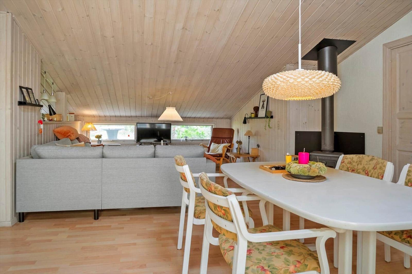 Ein Raum mit Essbereich und Wohnbereich unter Holzdecke. Es gibt eine Couch, einen Esstisch und einen Kamin.