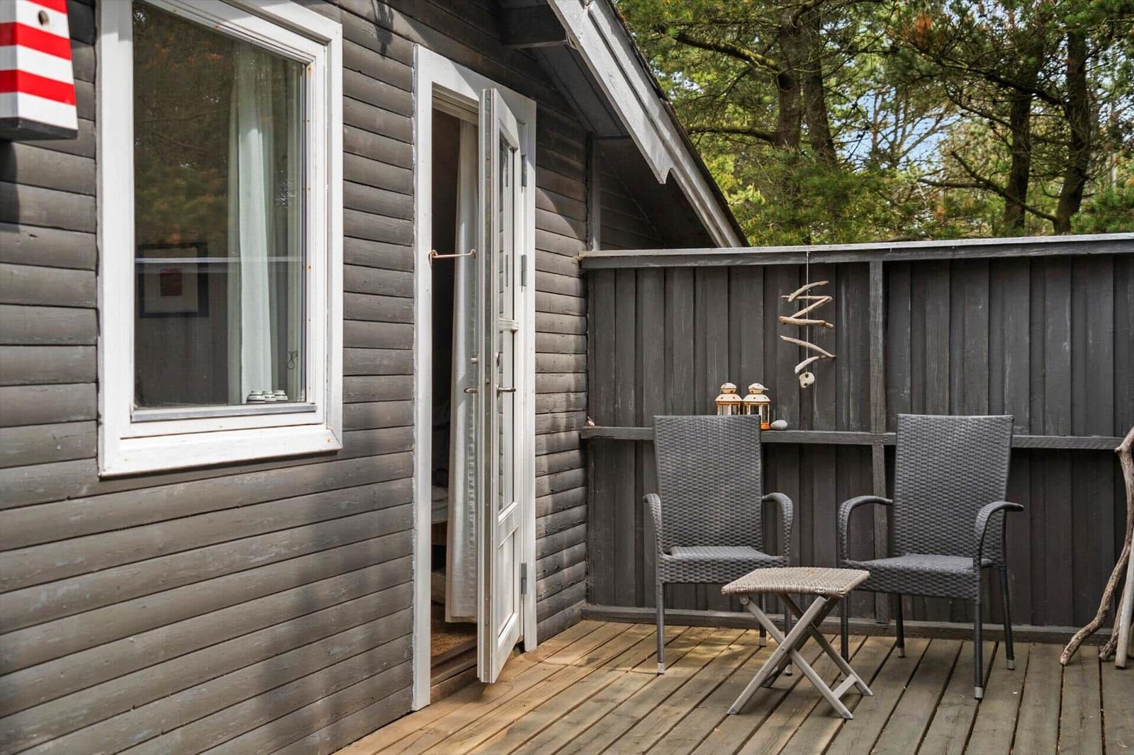 Terrasse mit zwei Stühlen und Tisch vor einem Haus mit Holzwand und offener Tür.