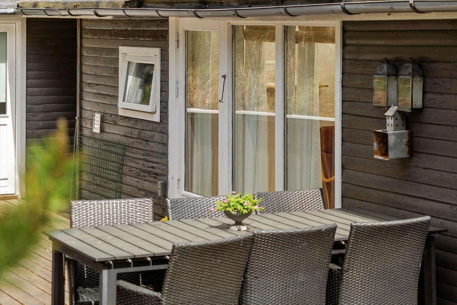 Terrasse mit Tisch und Stühlen vor einem Holzhaus mit Glastüren.