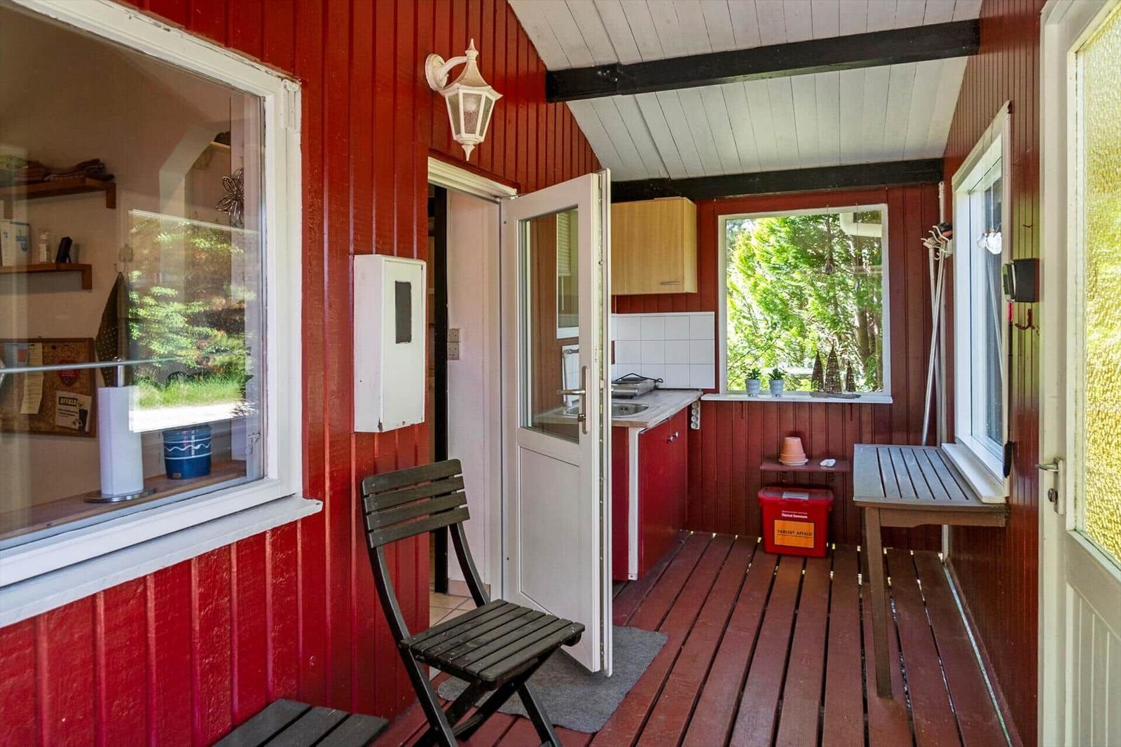 Roter Holzveranda mit Tisch, Stuhl und Blick in Küche.