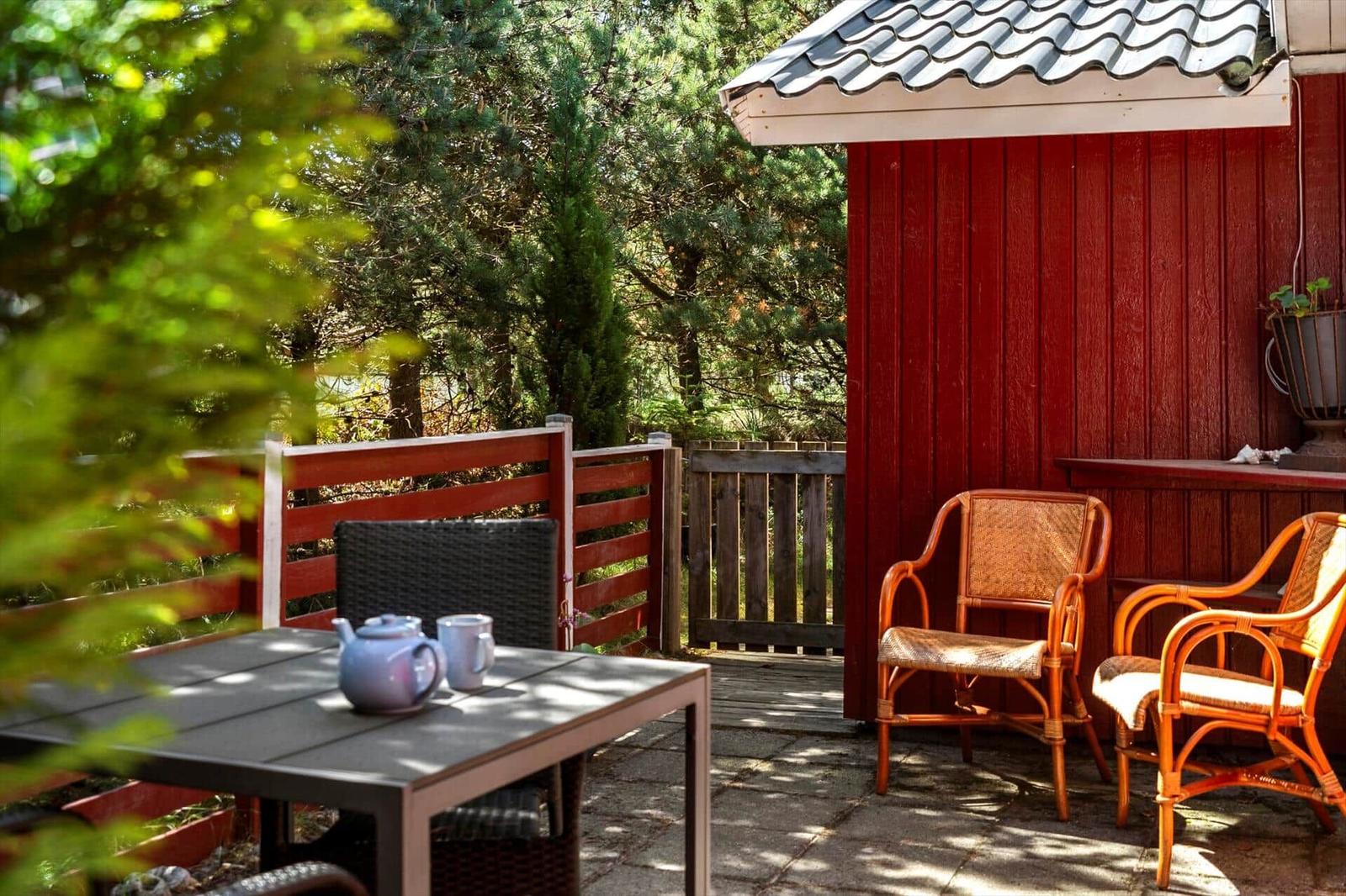 Terrasse mit Tisch, Stühlen und Blick auf grüne Bäume neben rotem Holzhaus.
