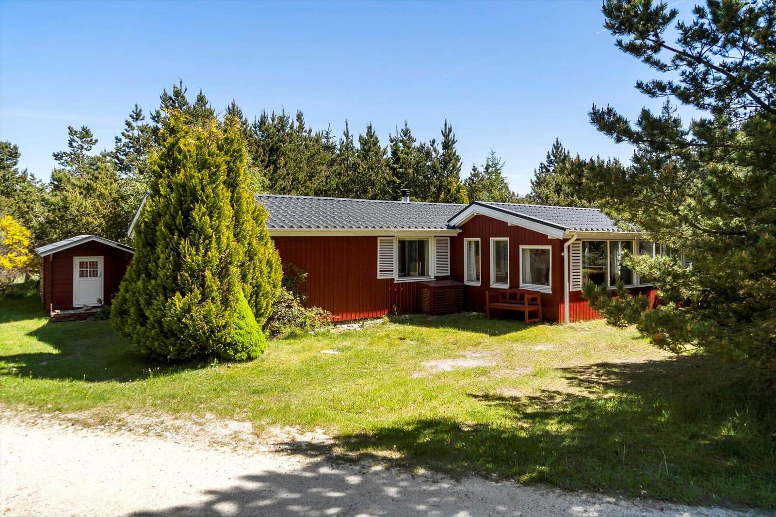 Rotes Holzhaus mit Schuppen und grünem Garten. Umgeben von Bäumen und einem klaren Himmel.