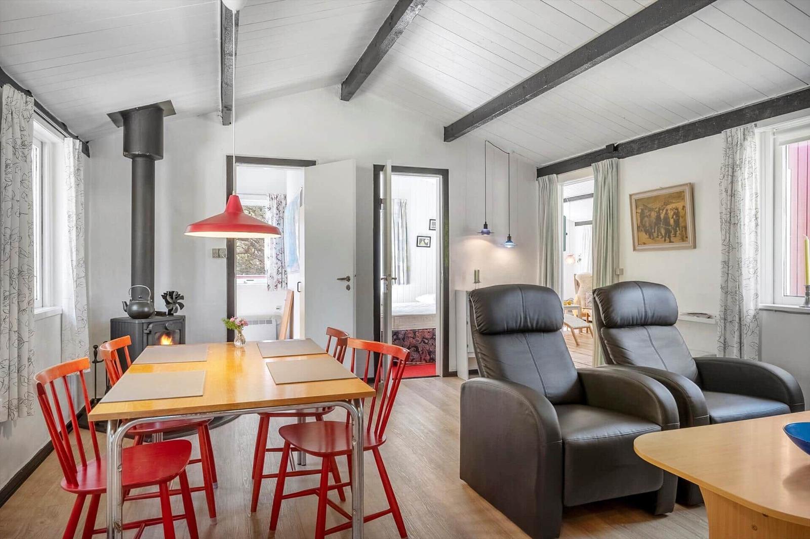 Essbereich mit Tisch und roten Stühlen, schwarze Ledersessel und Kamin im Wohnzimmer.