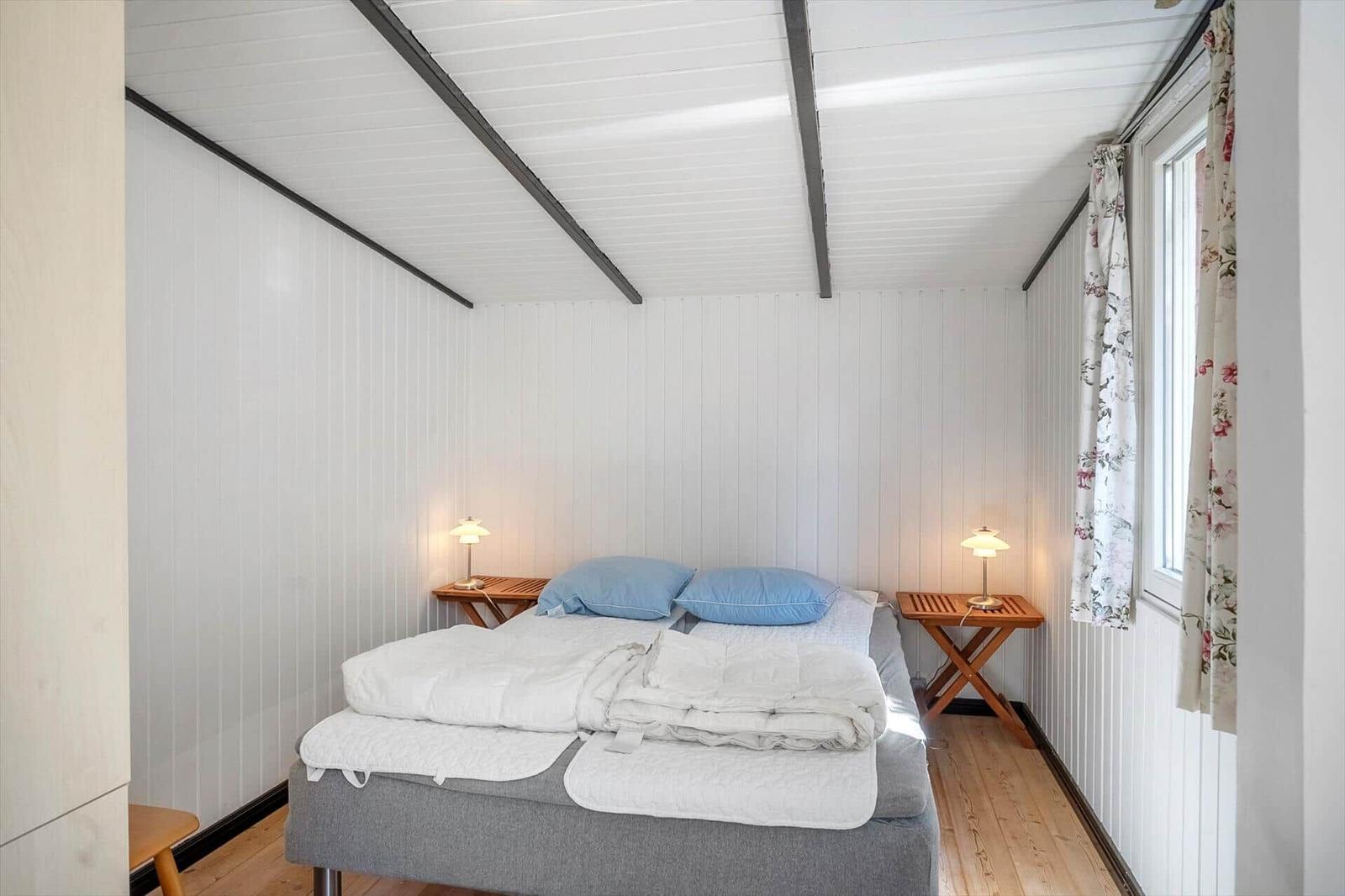 Schlafzimmer mit Bett, zwei Nachttischen und Fenster mit Vorhängen.